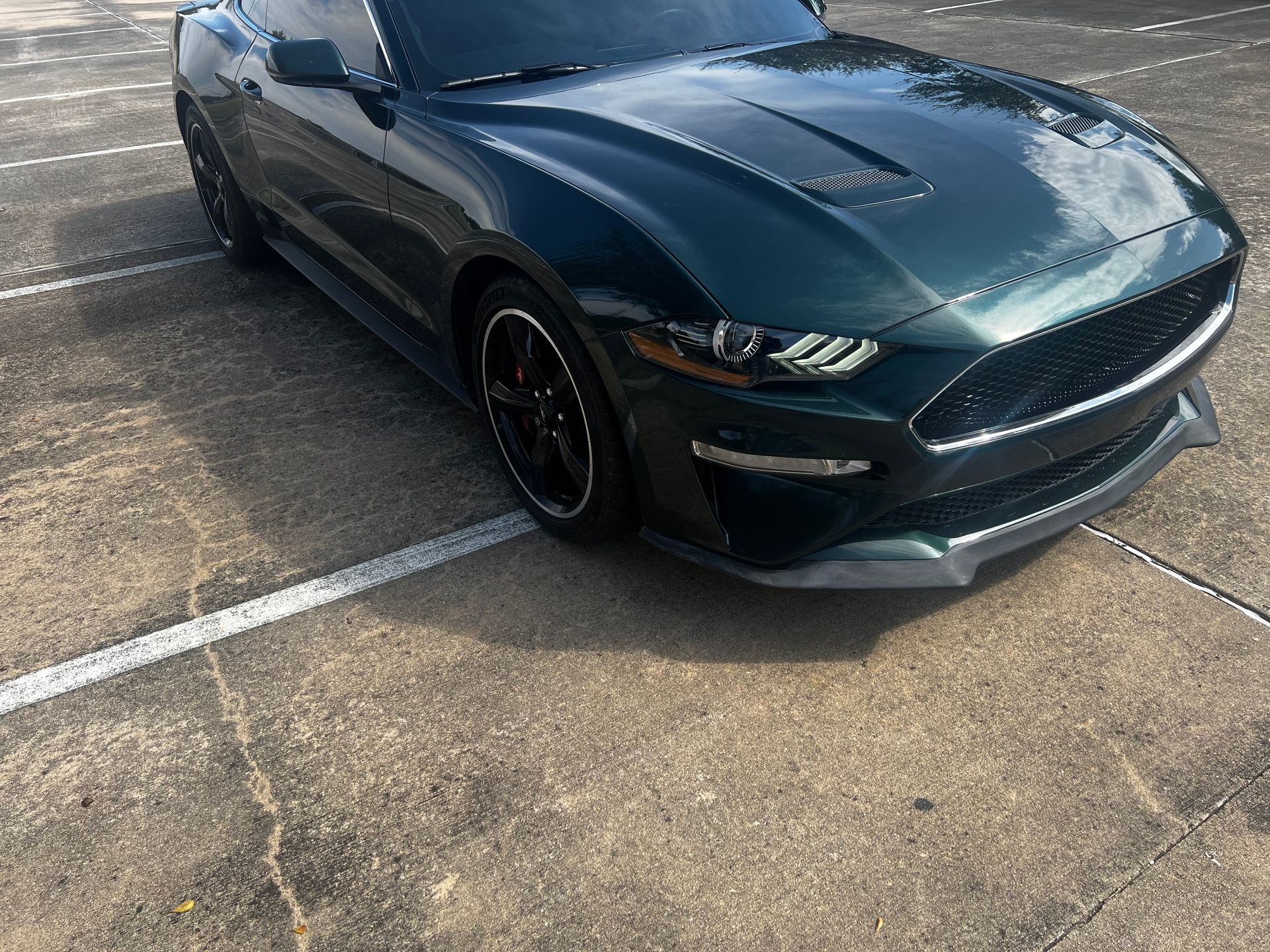 Dark green sports car parked in a lot, angled front view with black rims.