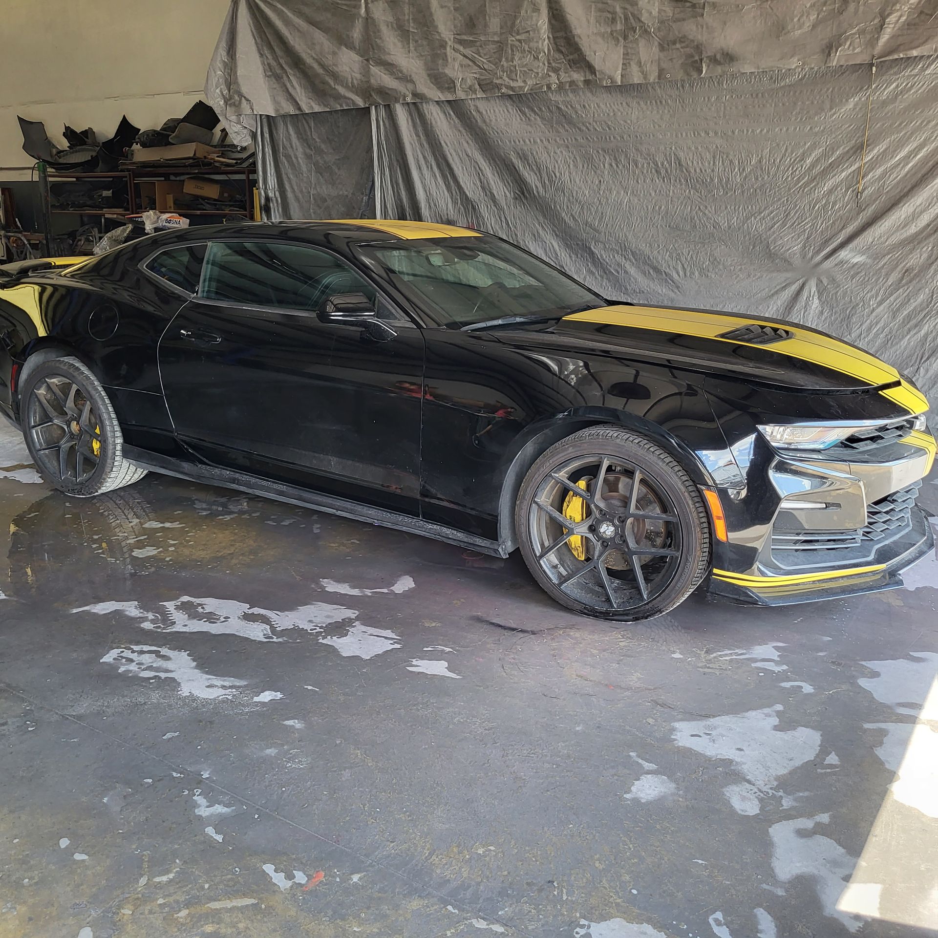 Black sports car with yellow accents parked in a garage, side view.
