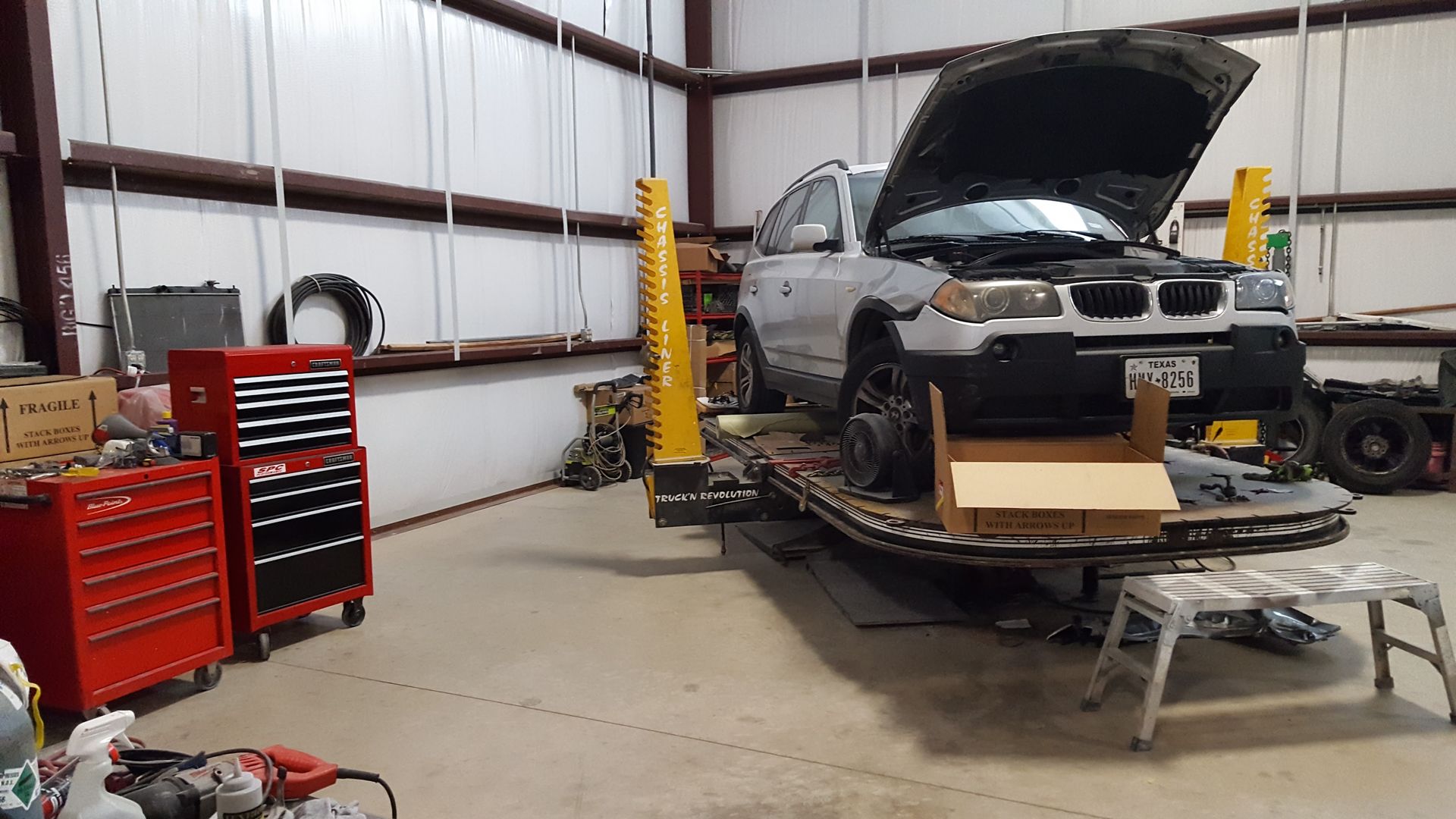 Car being repaired in a workshop, hood open, with tools and a red tool chest nearby.