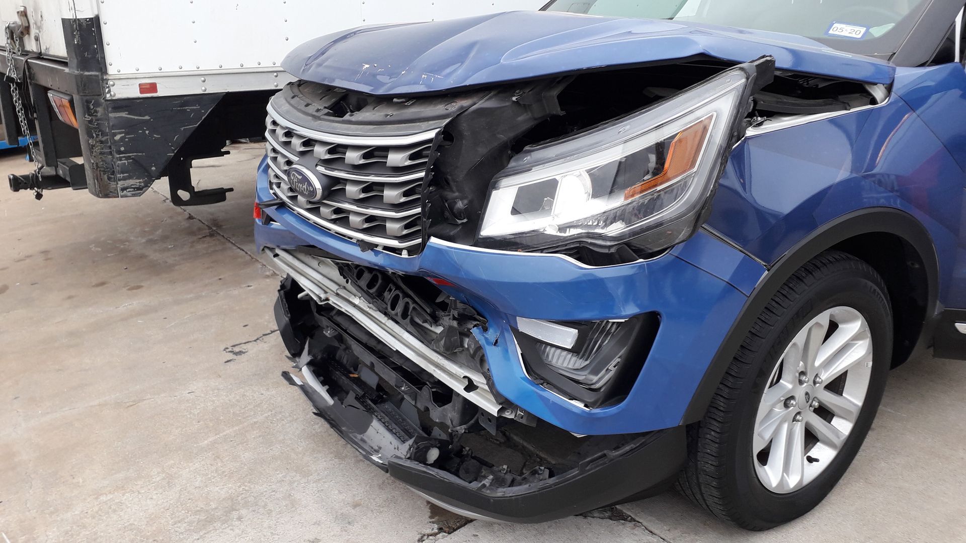 Blue SUV with severe front-end damage, missing bumper and grille, parked in a lot