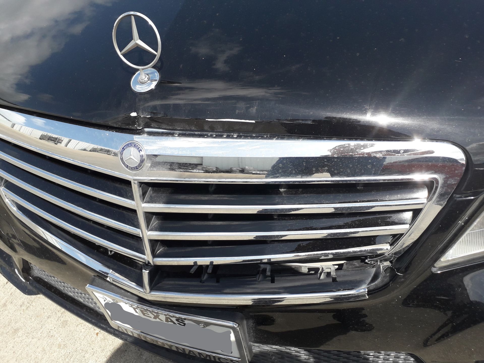 Close-up of a black Mercedes-Benz front grille with silver emblem and chrome trim, showing some damage and missing pieces
