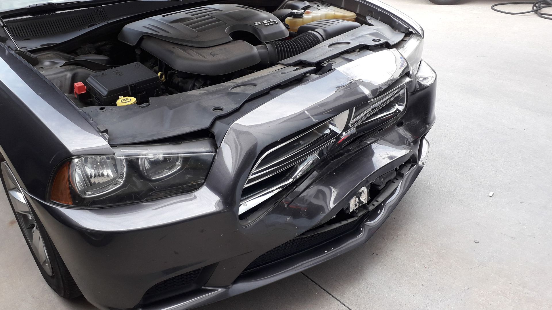 Damaged black car front with hood open, showing engine in a parking lot