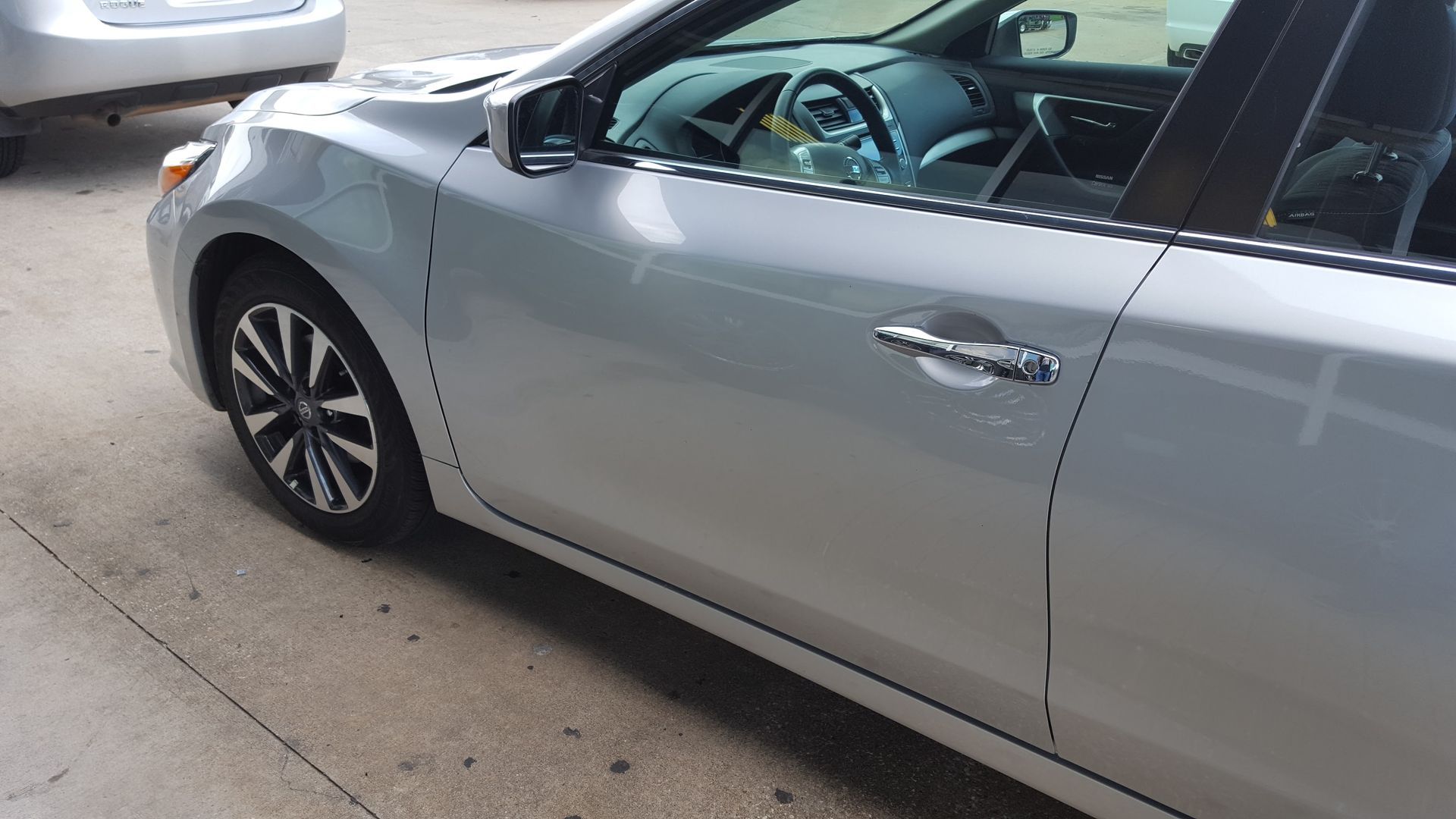 Silver sedan parked in a driveway, side view with front wheel turned slightly left