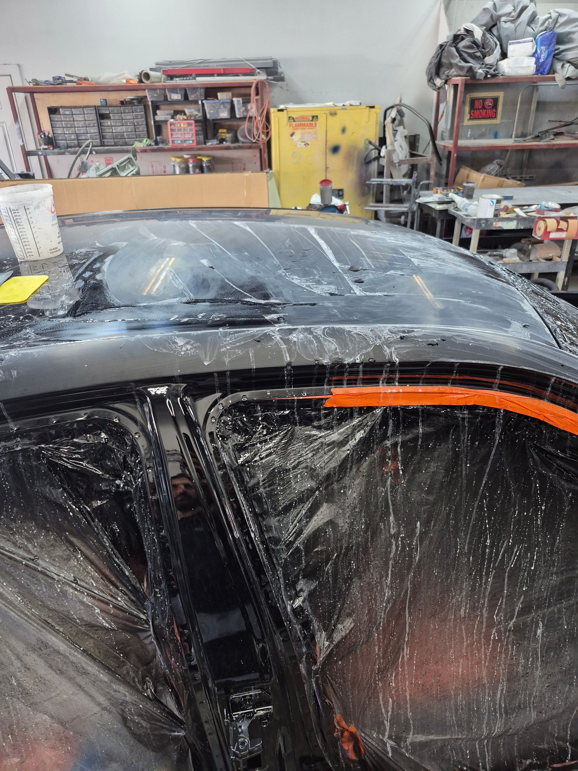Black car roof in an auto shop, covered in white soap suds with shelves and tools in the background