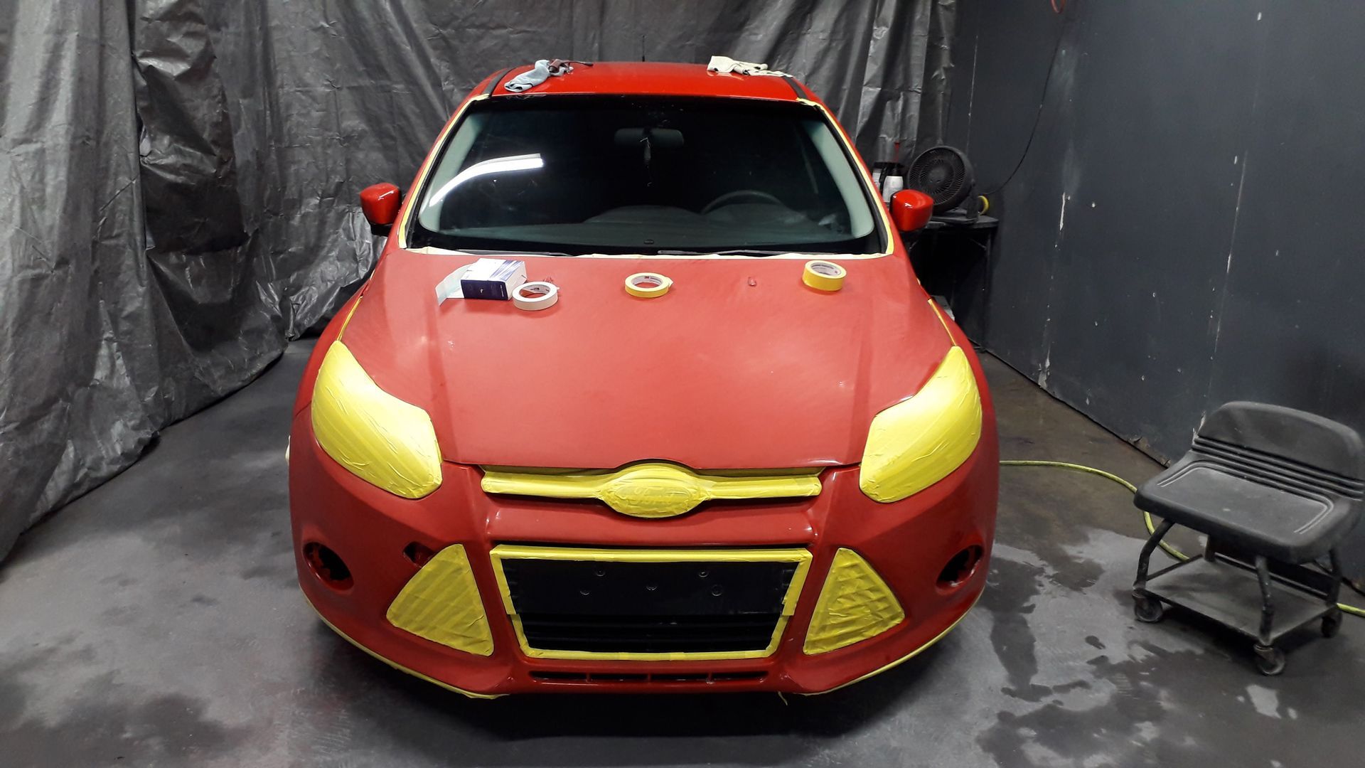 Red car with yellow headlights parked indoors on a studio floor next to a cart