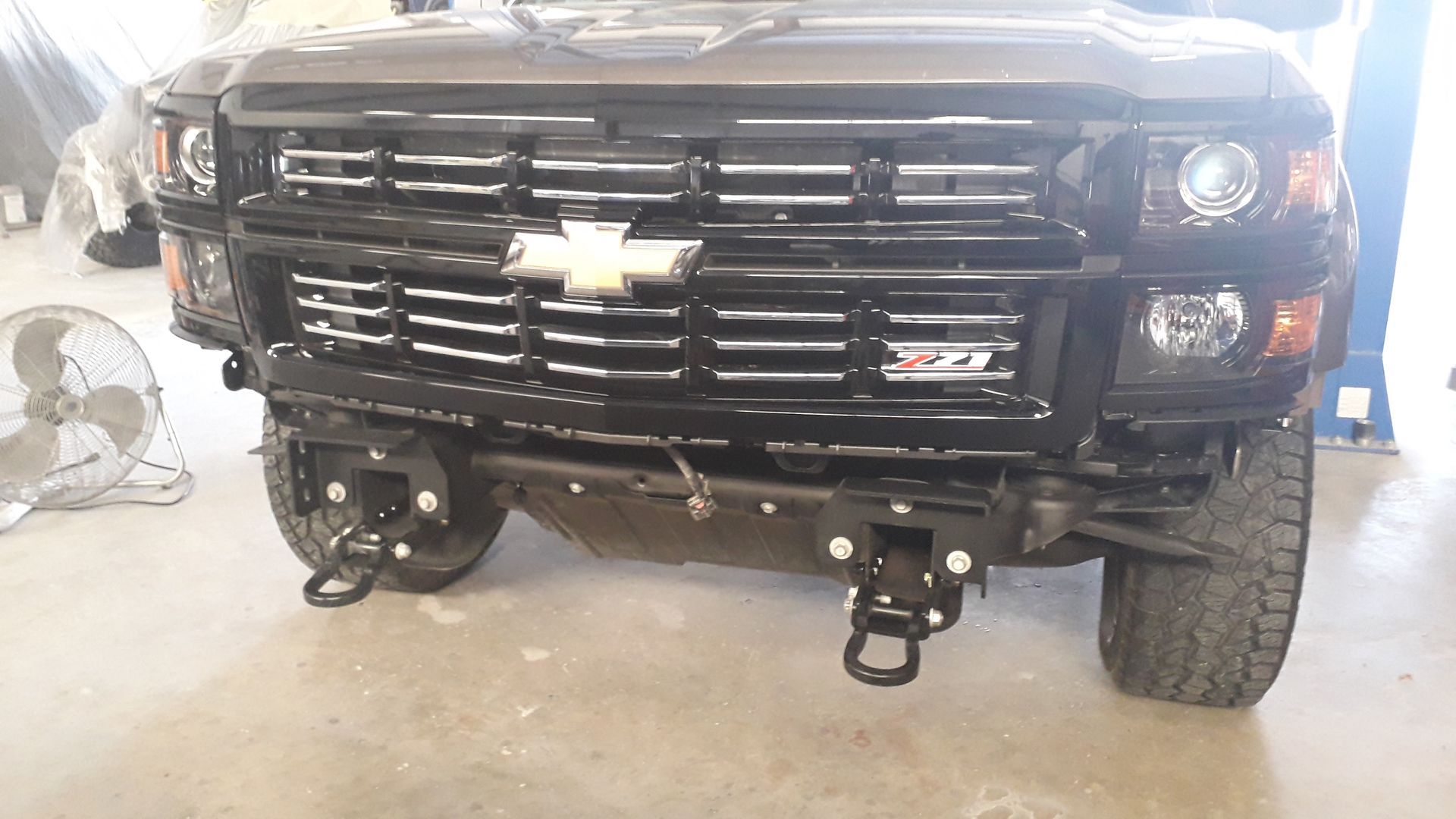Front view of a black Chevrolet pickup truck in a garage, with front bumper removed and tow hooks visible