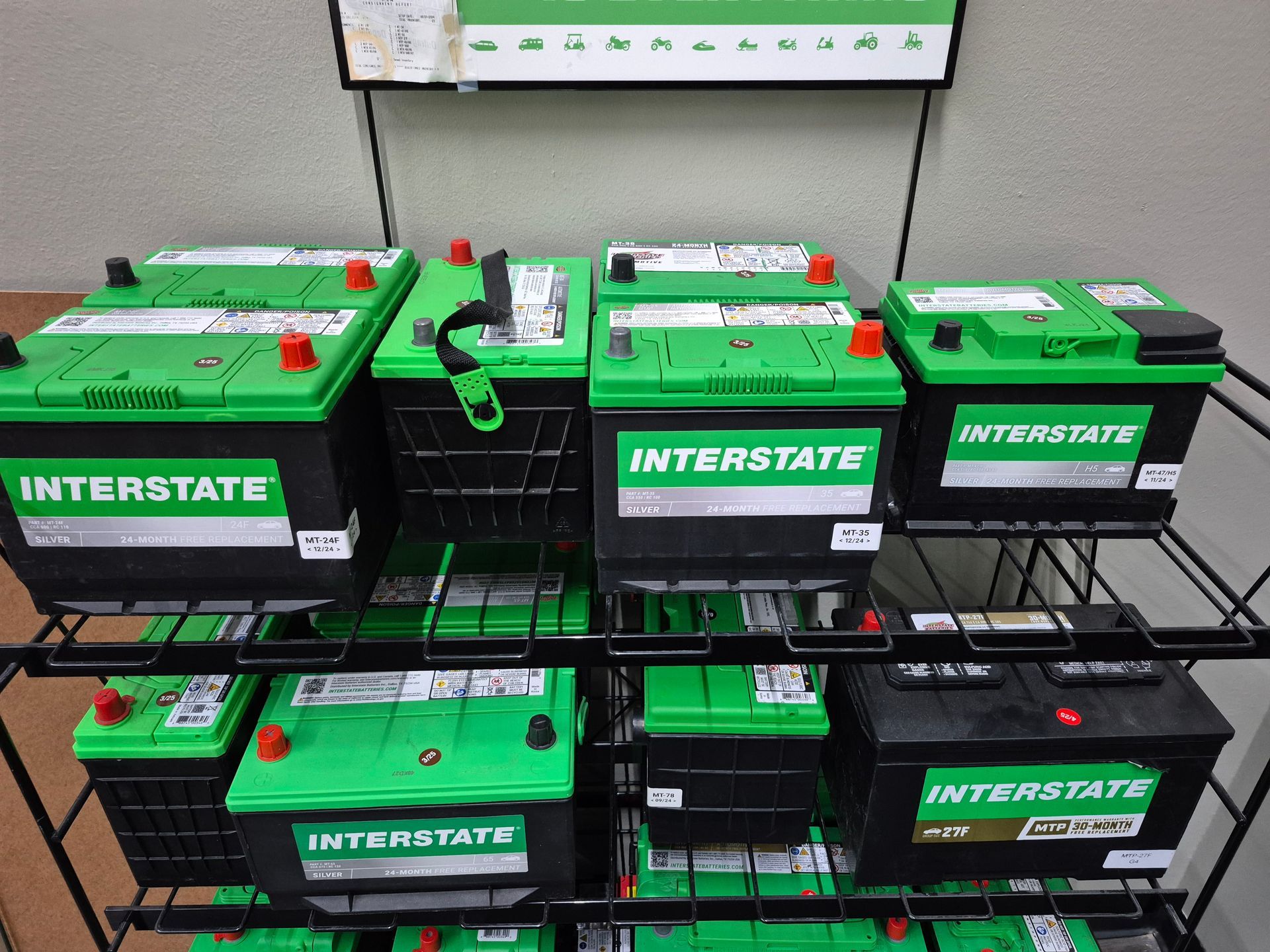 Stacked green Interstate car batteries on black shelving in a store.