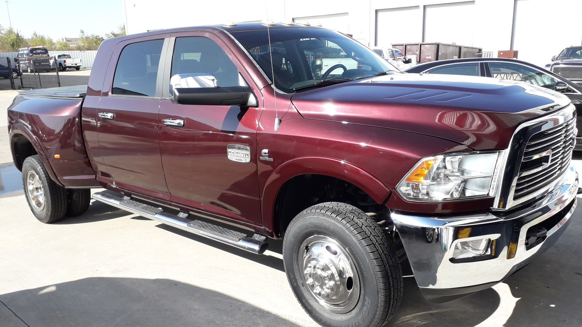 Maroon lifted pickup truck parked outdoors in a lot, front-right view, chrome grille visible