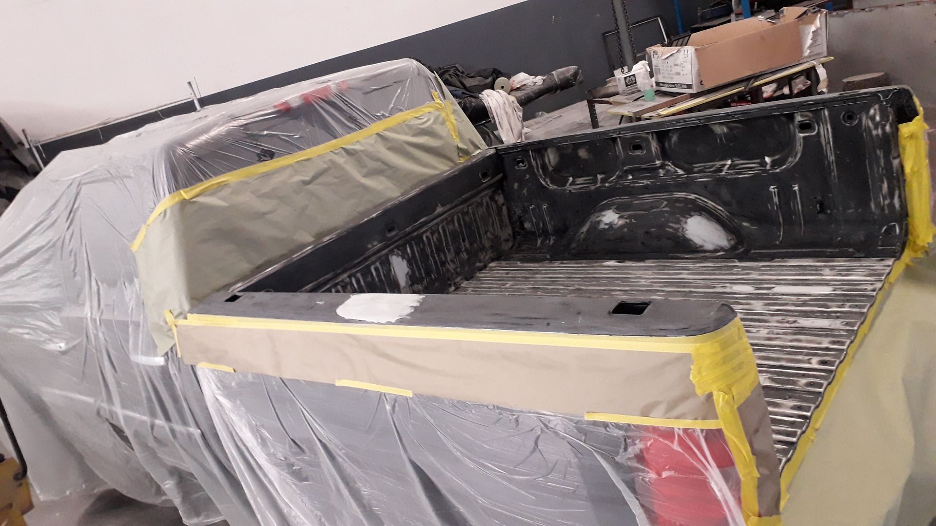 Pickup truck bed masked with plastic and tape, being painted in a workshop