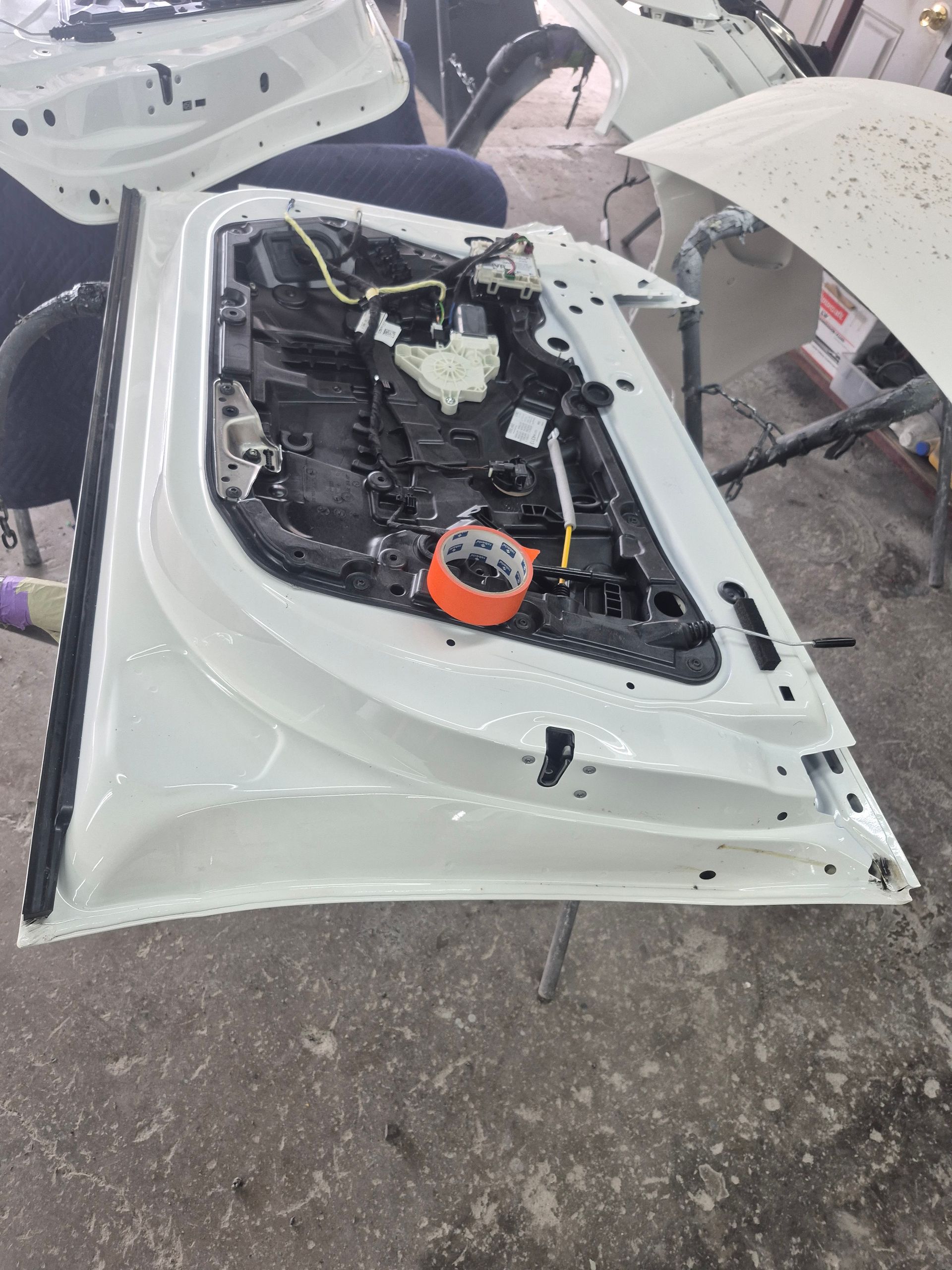 White car door frame in a workshop, showing exposed black interior components and a red-ringed part.