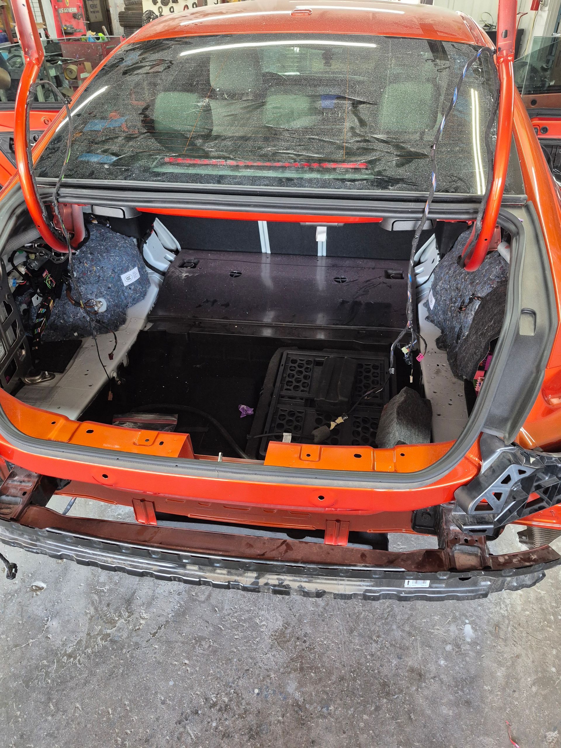 Orange car body stripped to the frame in a repair shop, with the hood and interior removed.