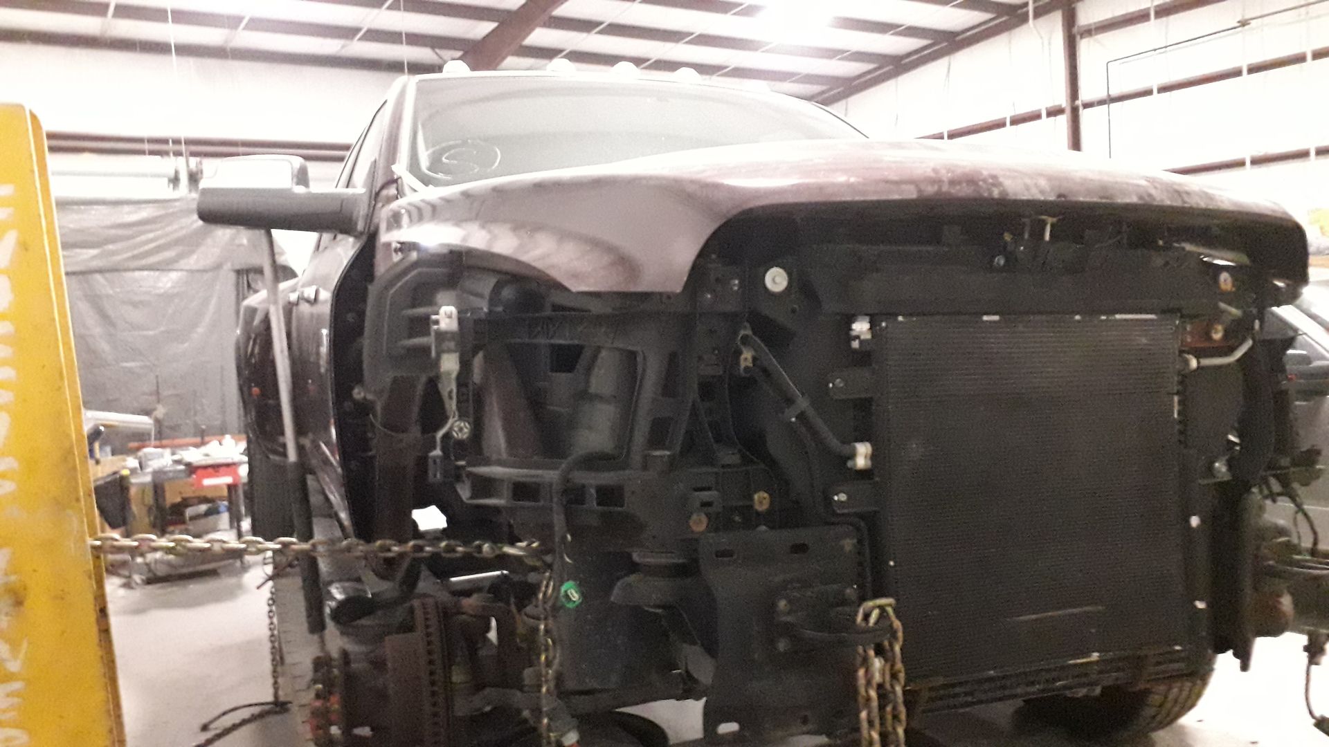 Front view of a silver car with the bumper removed in a garage, exposing the radiator and front frame.