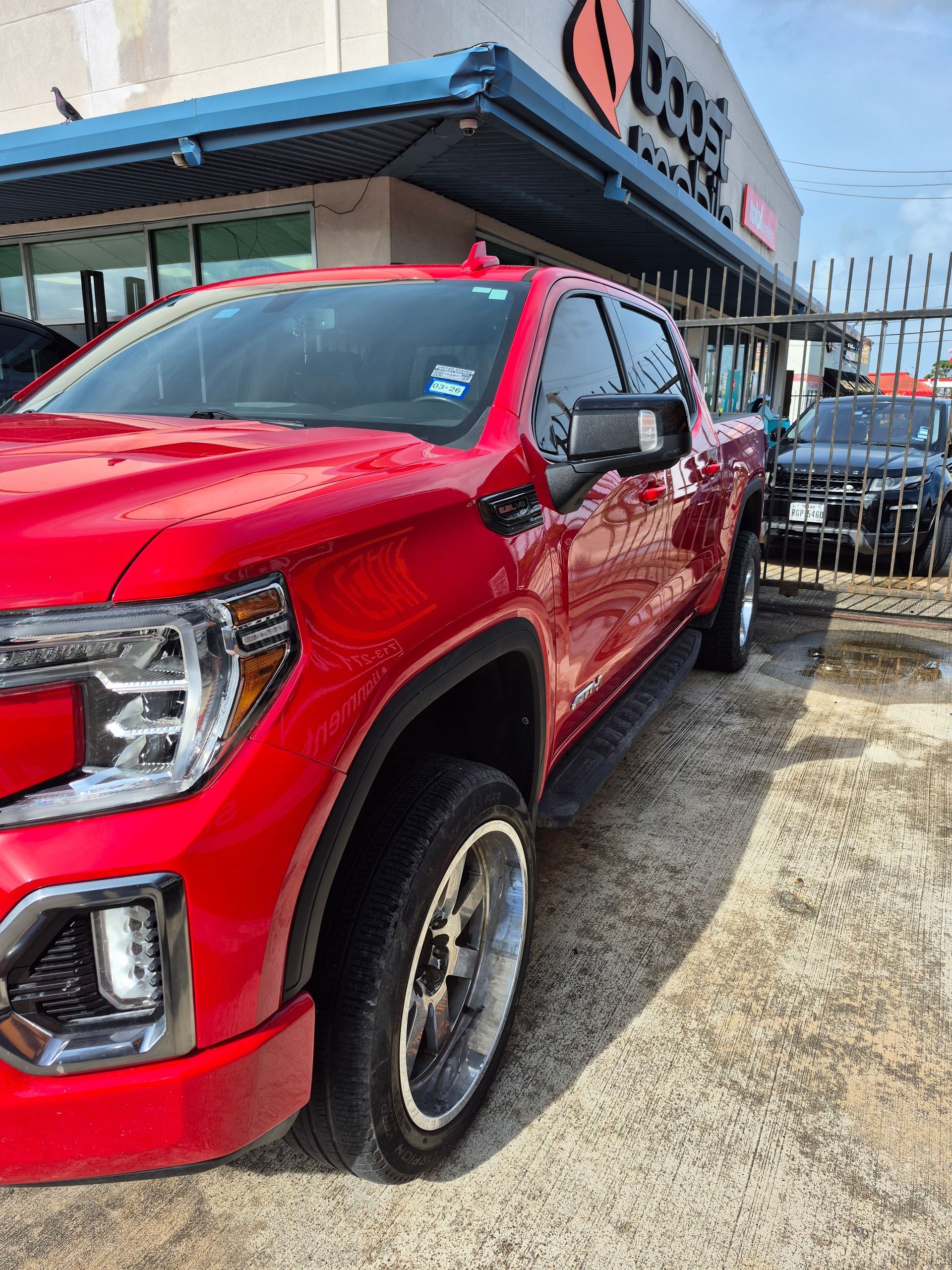 Red pickup truck parked outside a storefront on a sunny day