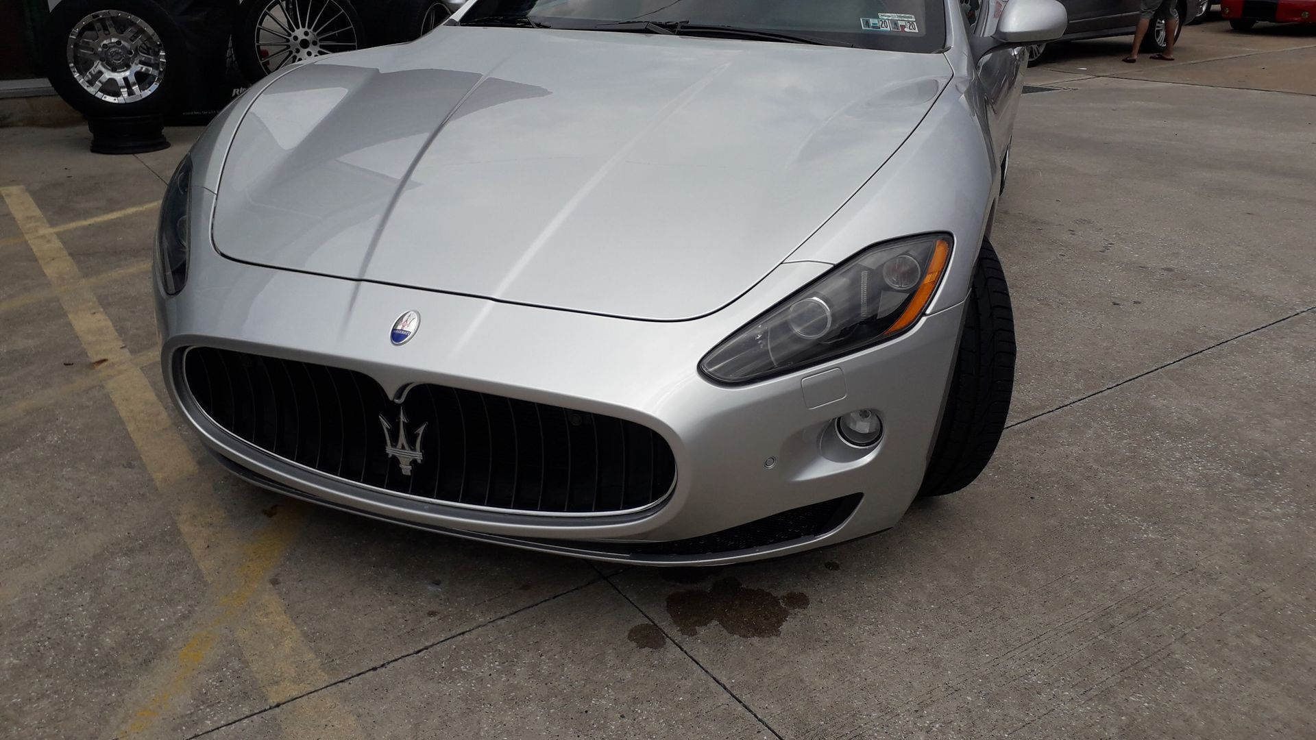 Silver Maserati sports car parked on pavement, front view with grille and headlights visible