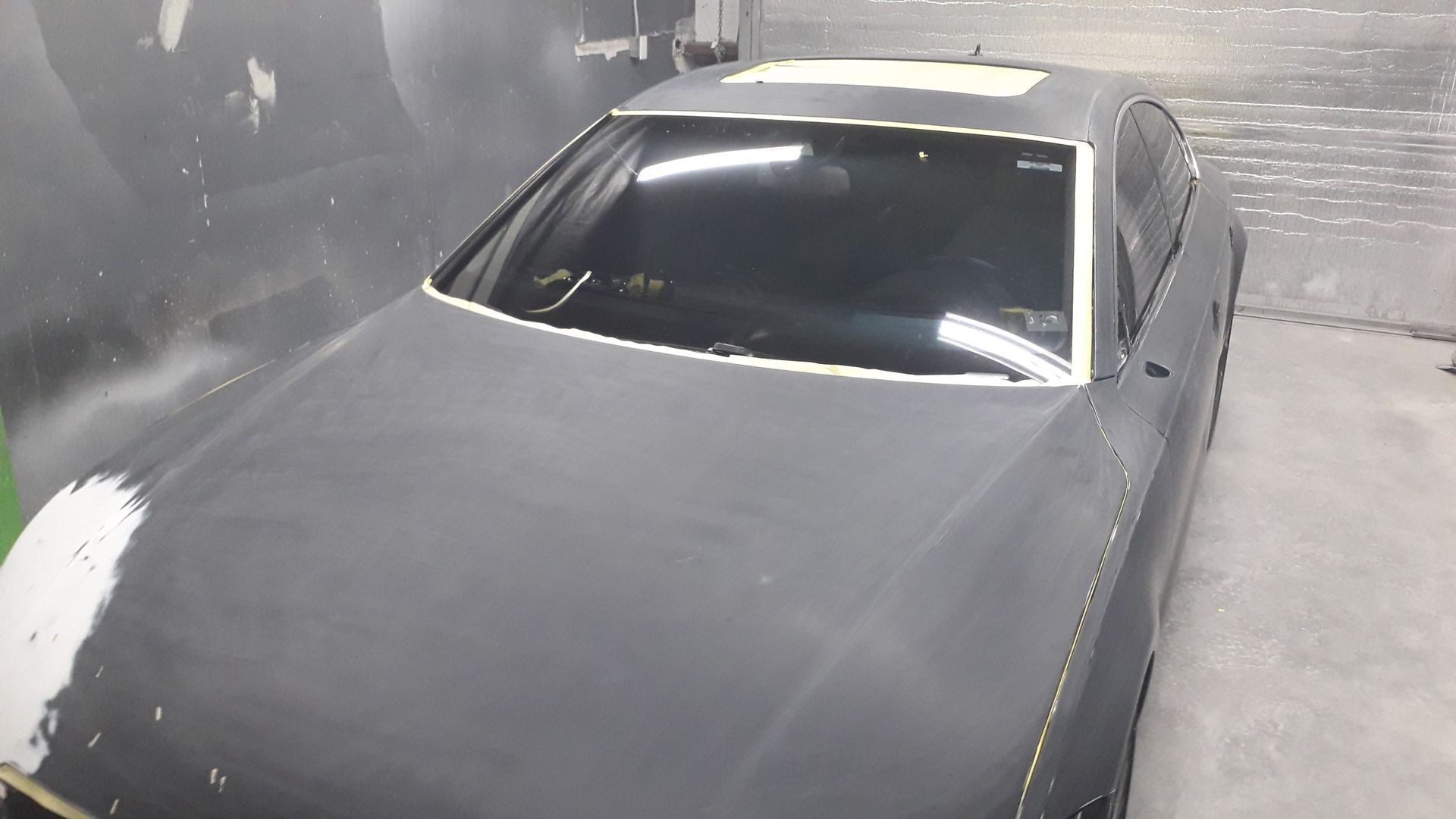 Gray car in a dusty spray booth, viewed from above with hood and windshield visible.