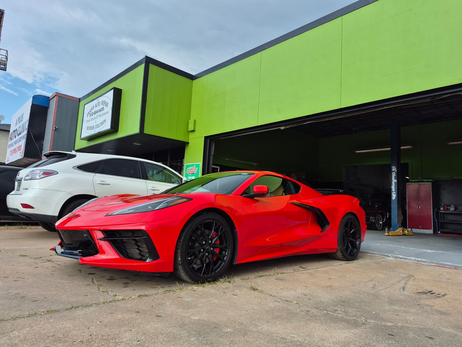 Red sports car parked outside a green auto shop, with a white car nearby.