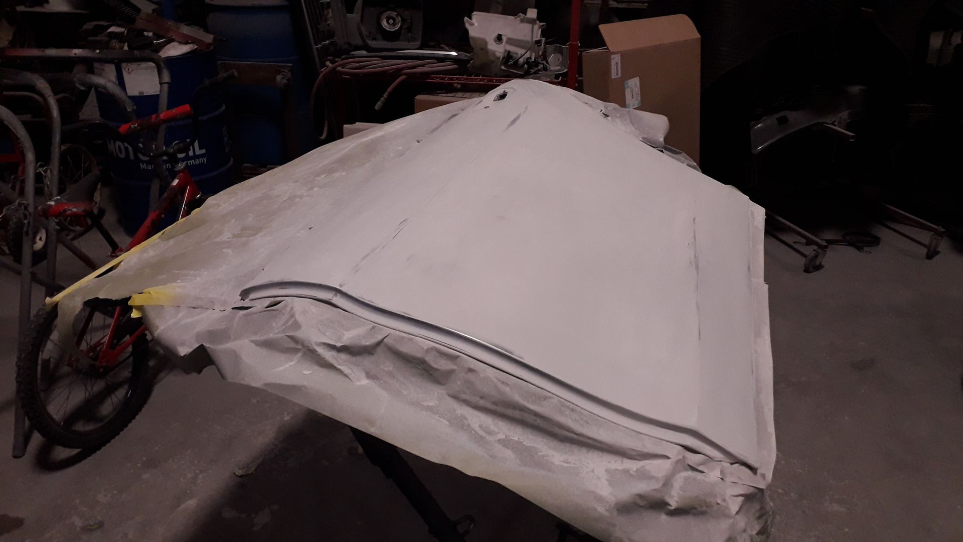 White tarp-covered object in a garage or workshop, with a bike partially visible on the left.
