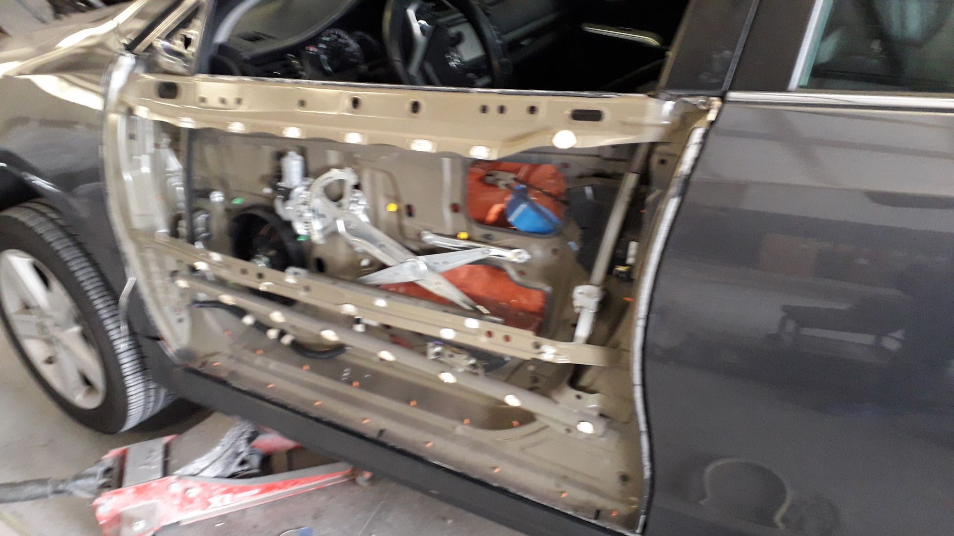 Car door panel removed, exposing white frame and red components during repair