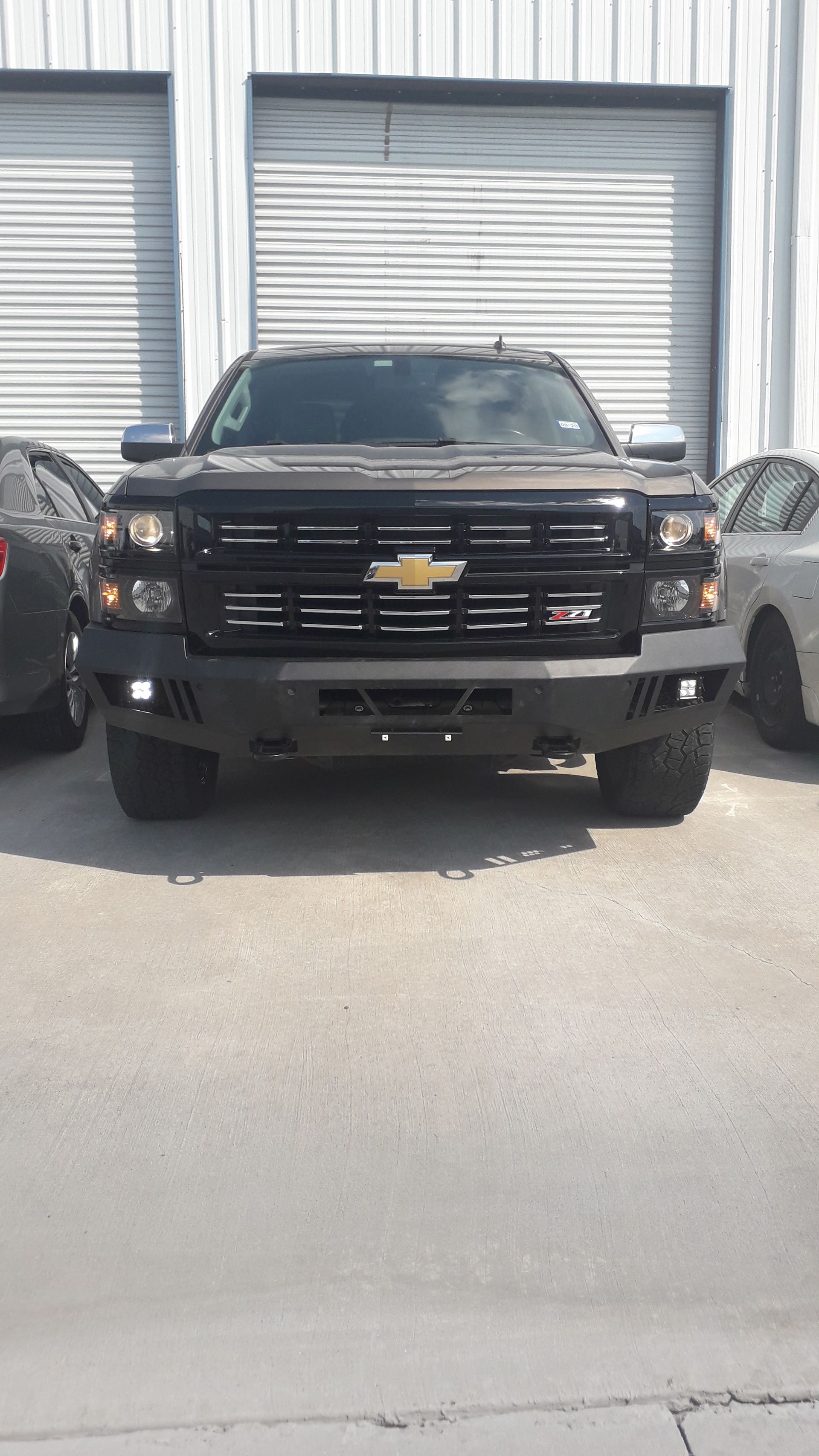 Black Chevrolet pickup truck parked in front of closed garage doors, viewed from the front.