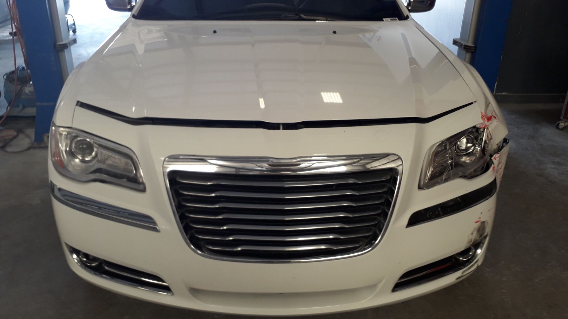 Front view of a white Chrysler sedan in a garage, showing the grille and headlights
