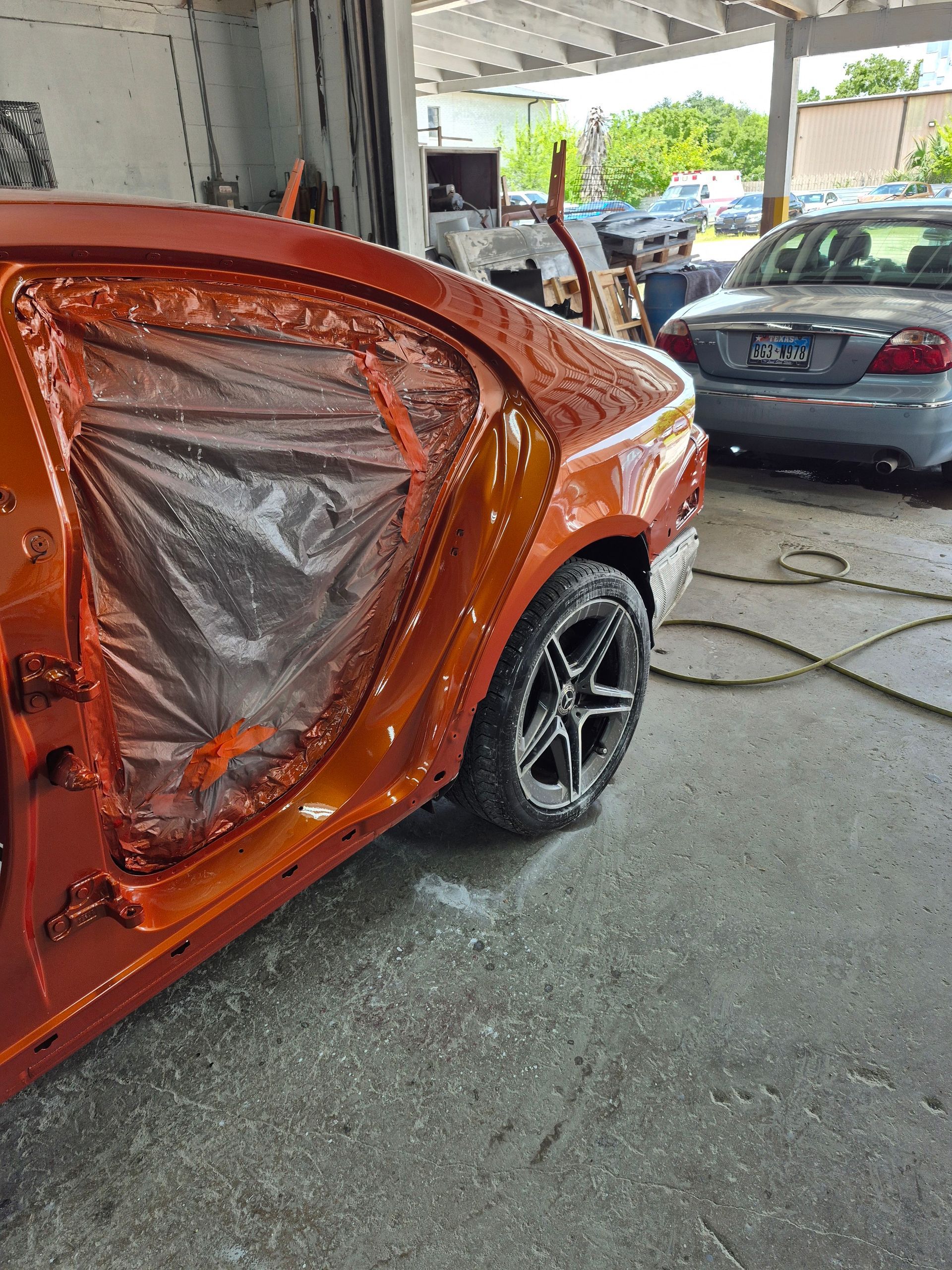 Orange car with rear door covered in plastic wrap in an auto body shop