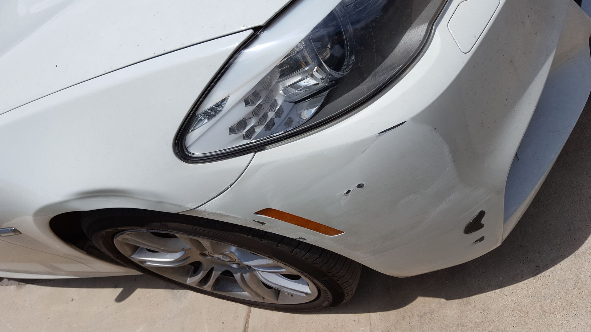 Close-up of a silver car’s front fender and wheel with a small scratch near the headlight