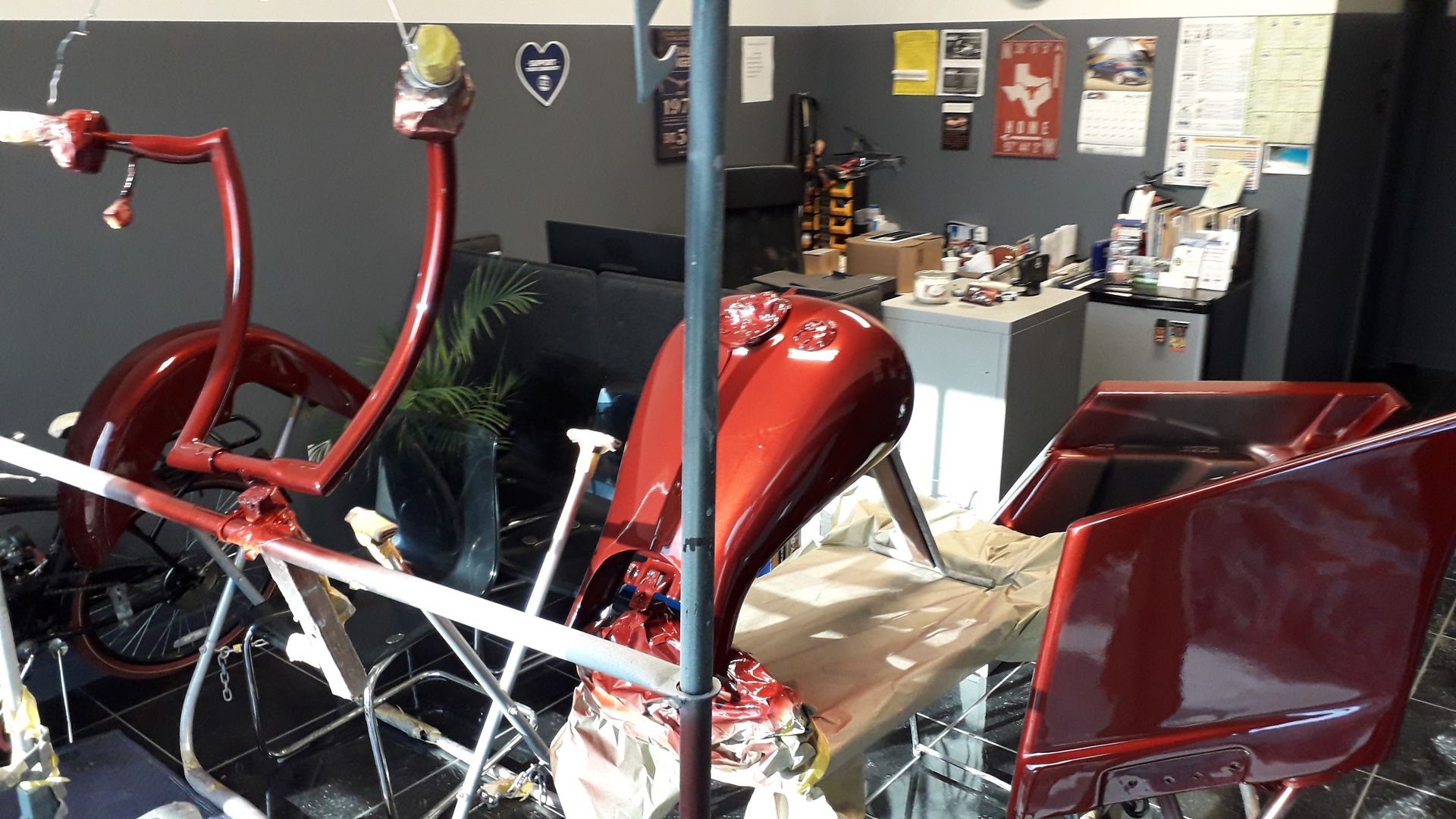 Red custom trike or motorcycle on display in a shop, with shiny bodywork and tall handlebars.