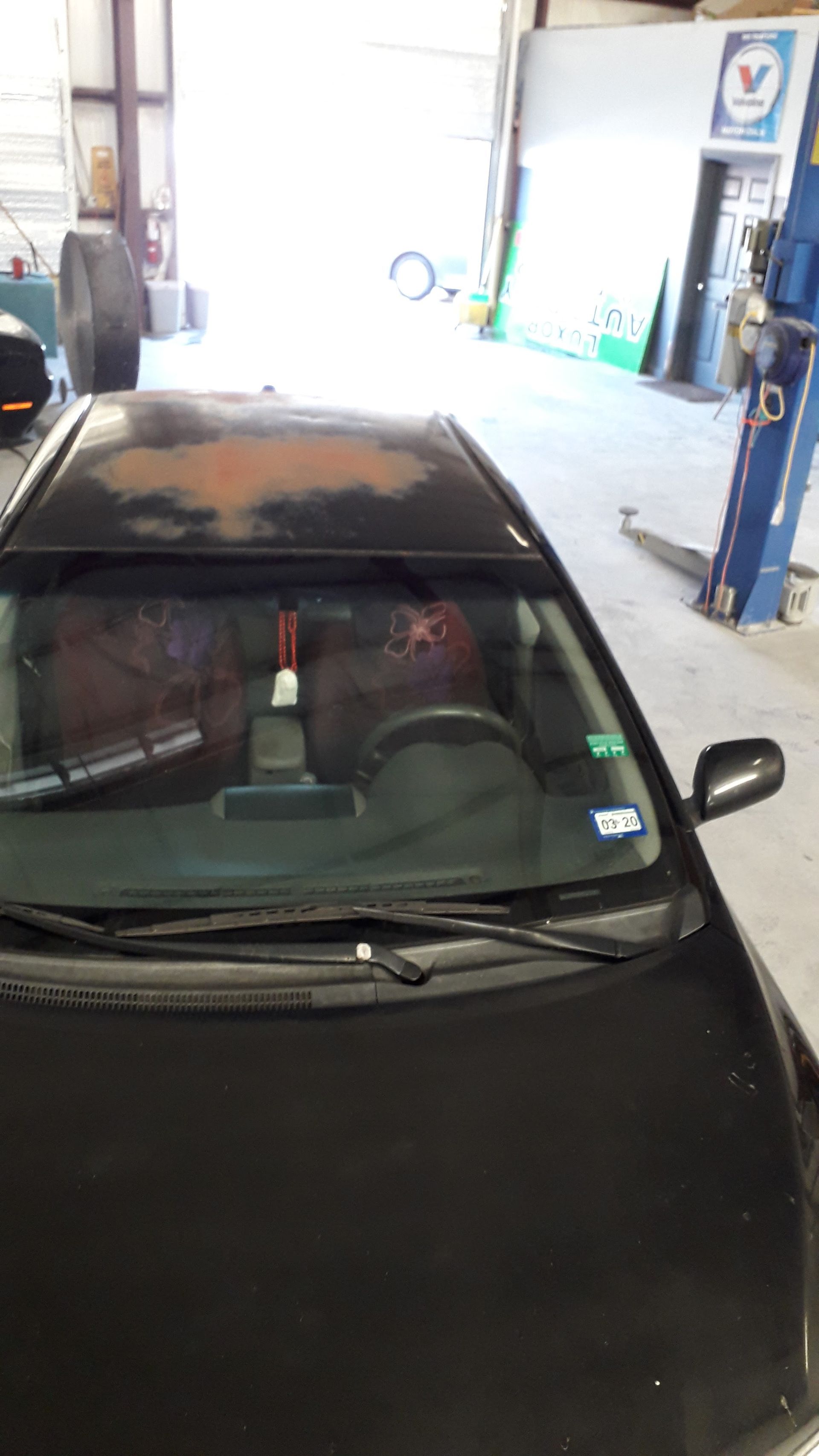 Black car inside an auto repair garage, seen from above at the front windshield.