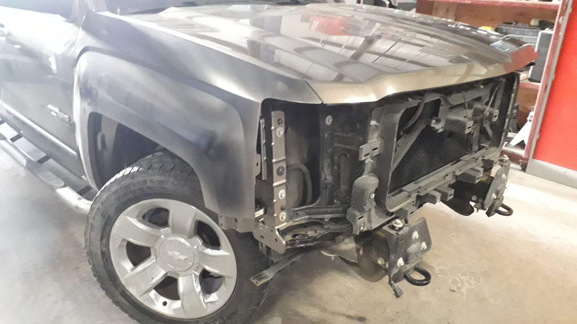 Black pickup truck with severe rear-end damage in a repair shop, exposed frame and bumper parts removed