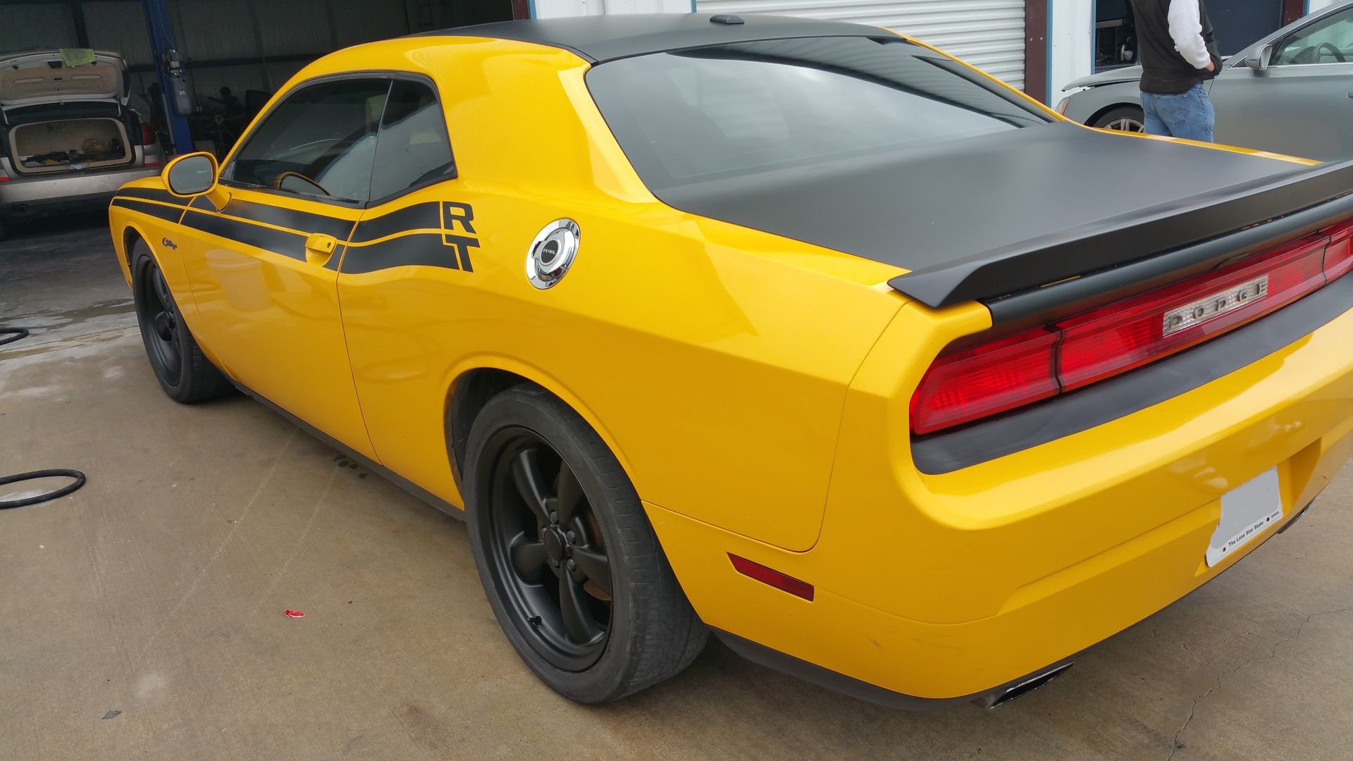 Yellow sports car with black racing stripes, parked outdoors, rear three-quarter view