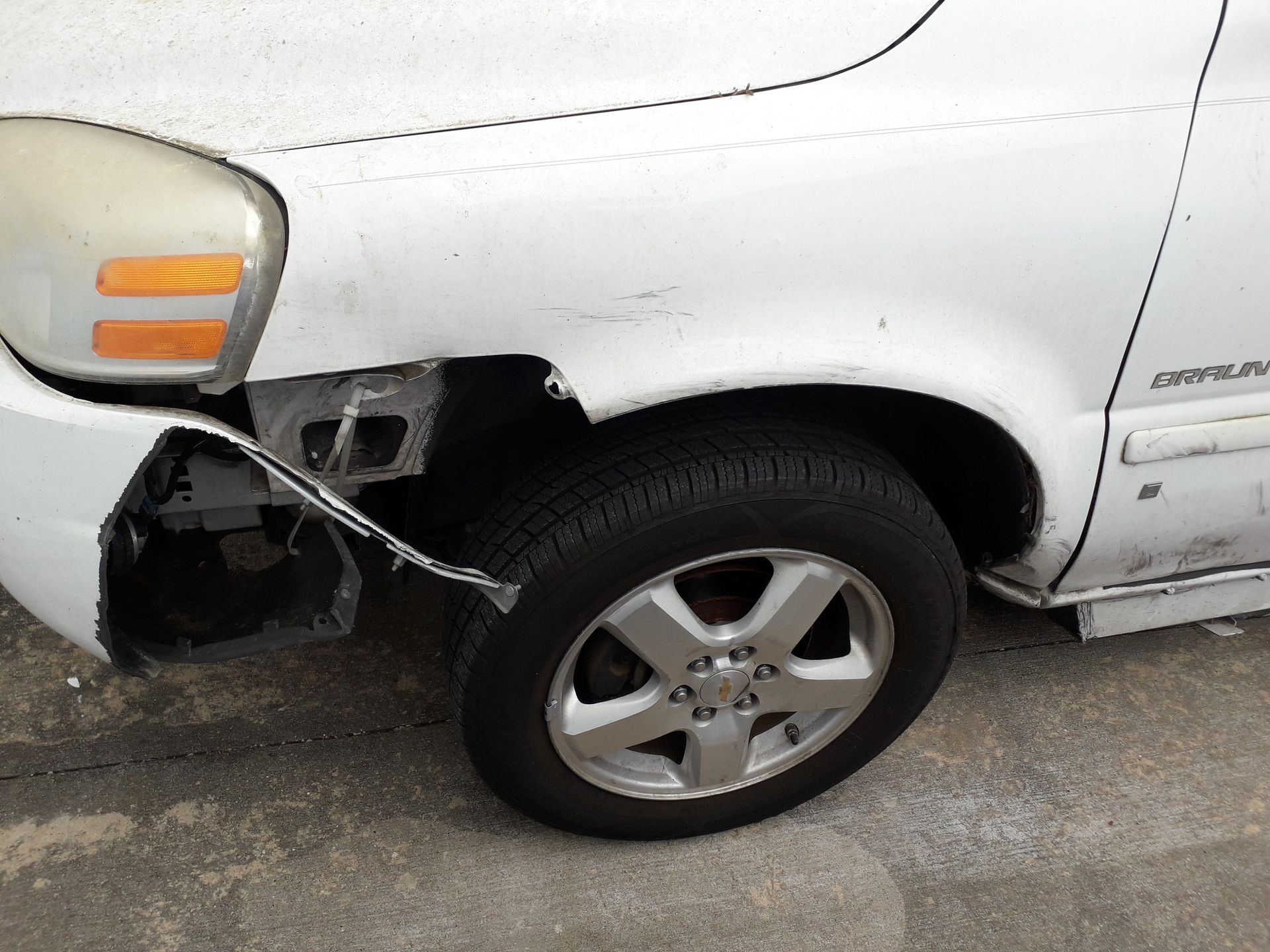 Damaged white pickup truck front fender and bumper near front wheel, with dangling broken trim