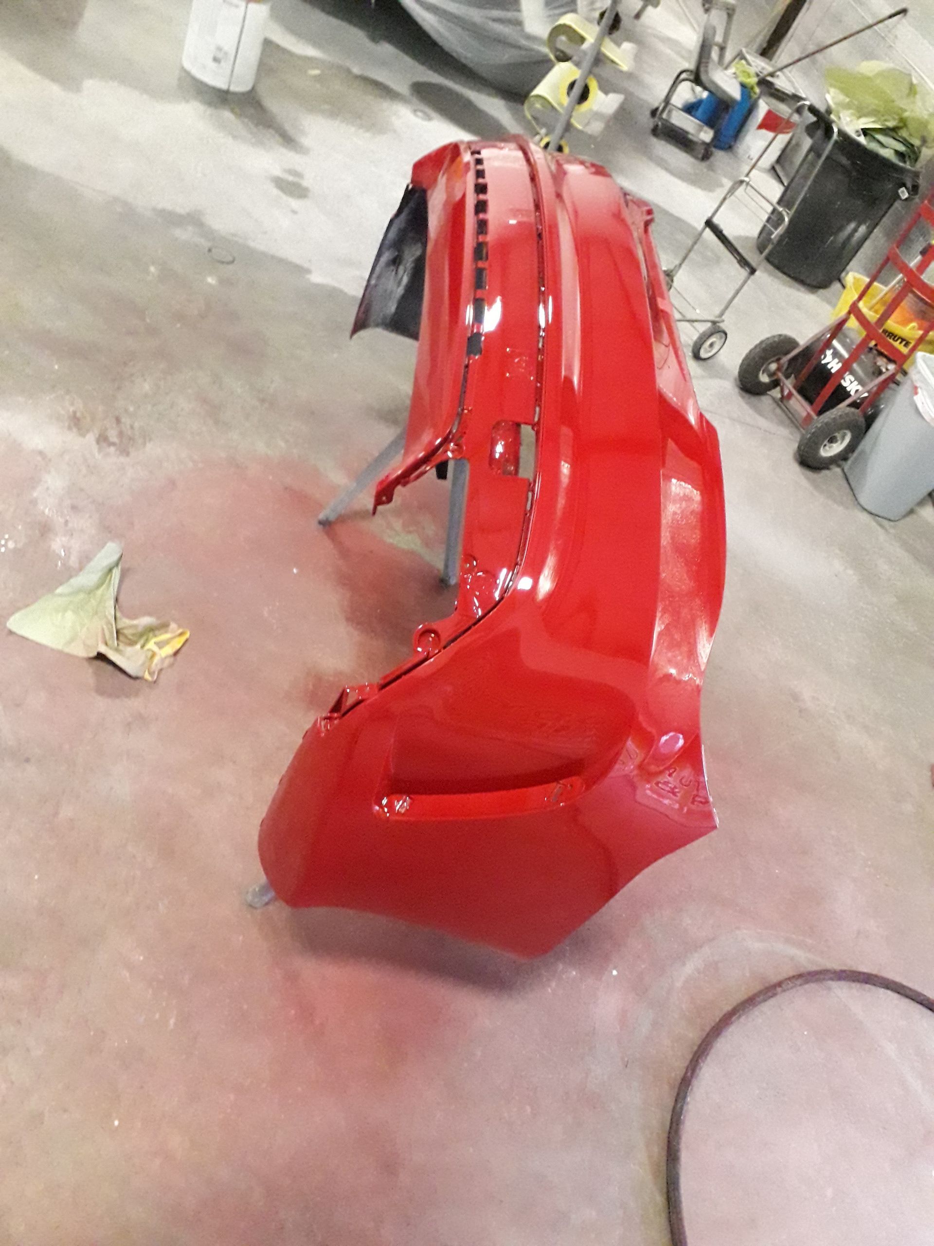 Red car bumper in a workshop, freshly painted and standing upright on the floor.