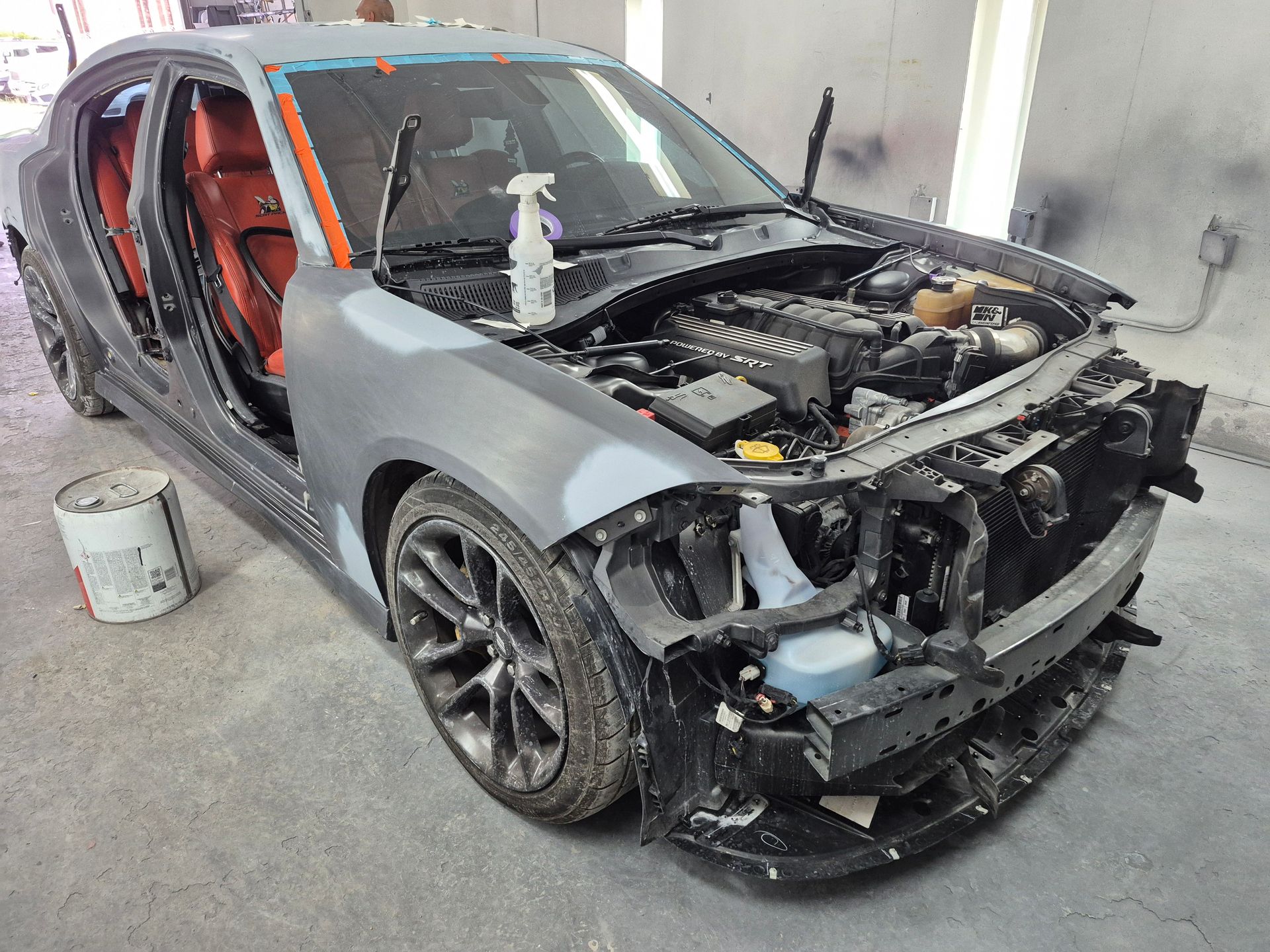 Damaged gray sports car with front-end collision damage in a garage, hood open and door removed