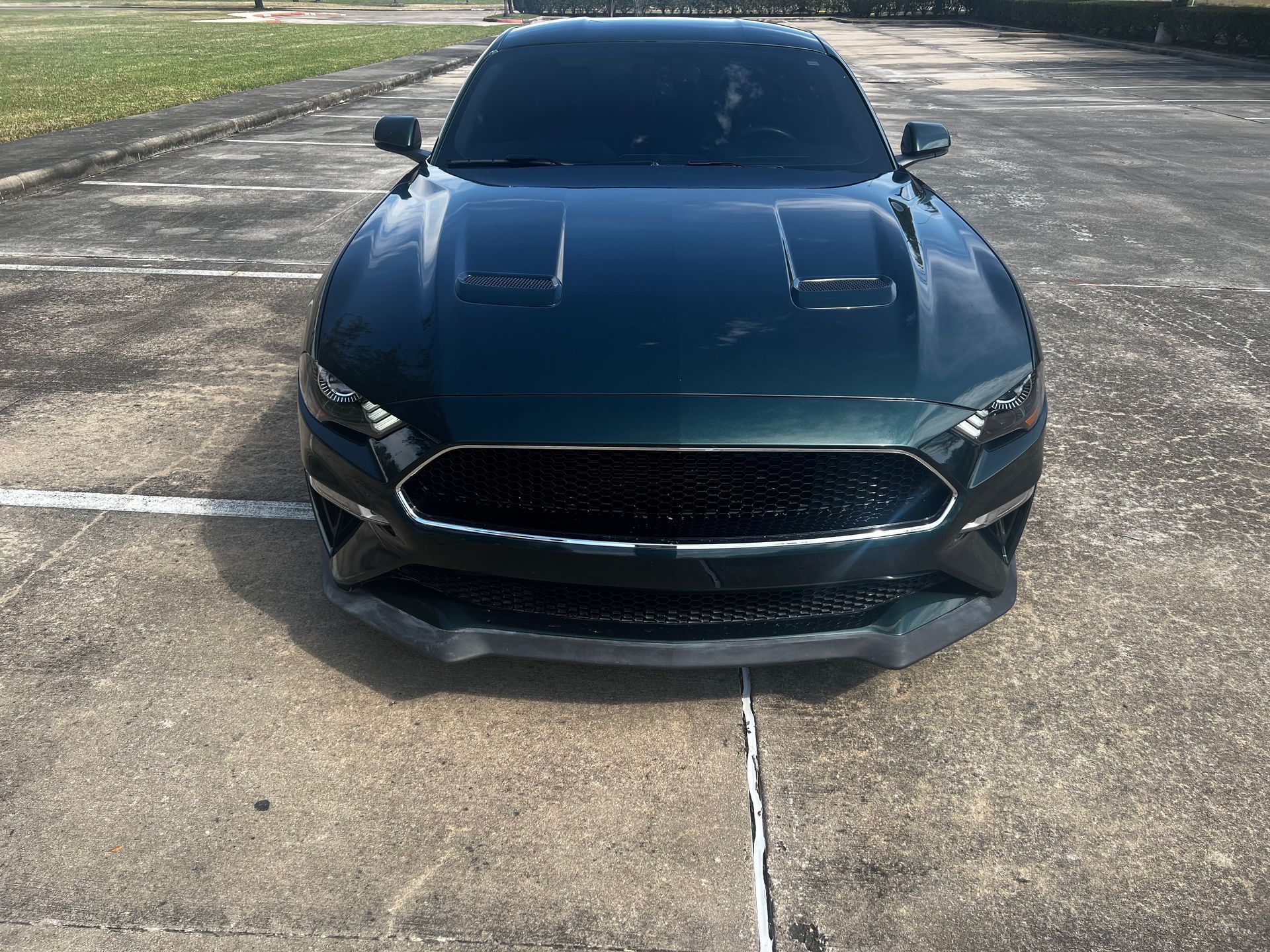 Dark green sports car parked on a cracked parking lot, front view.