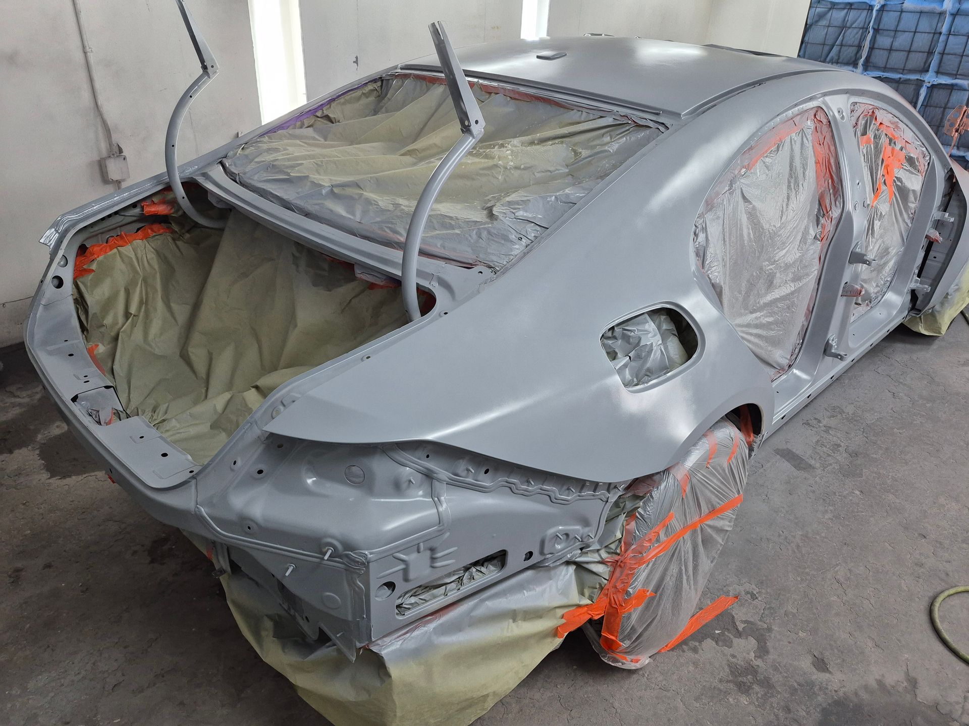 Gray car body shell in a workshop, with missing windows, wheels removed, and exposed orange suspension parts