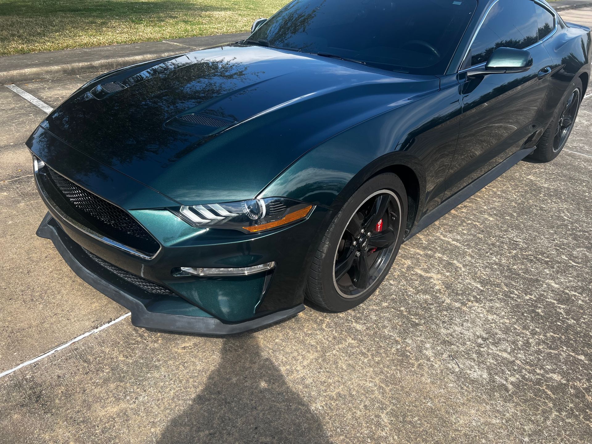 Dark green sports coupe parked on a paved lot, front-left angle view, with black wheels.