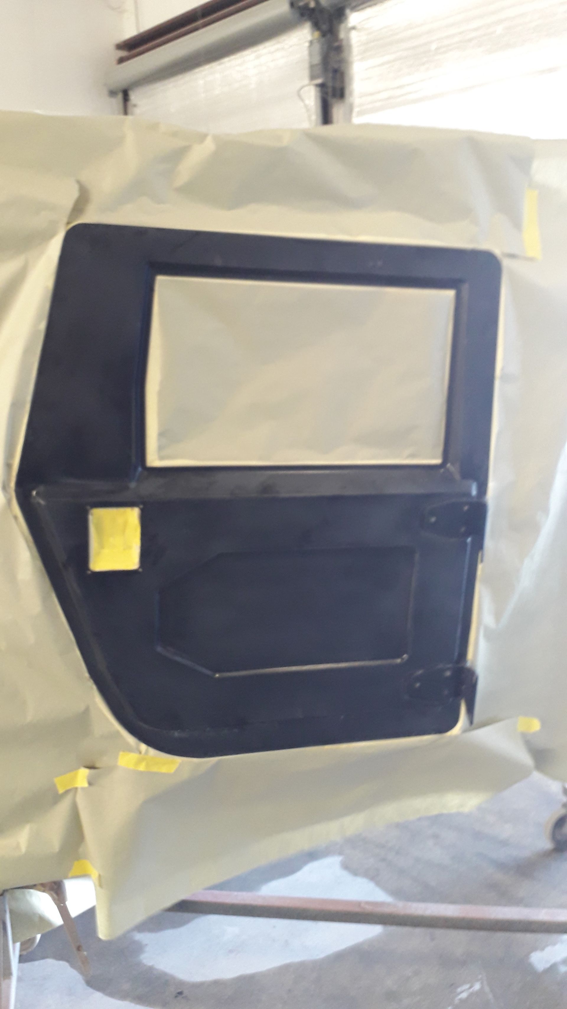 Dark blue car door panel masked with plastic and tape in a workshop spray booth