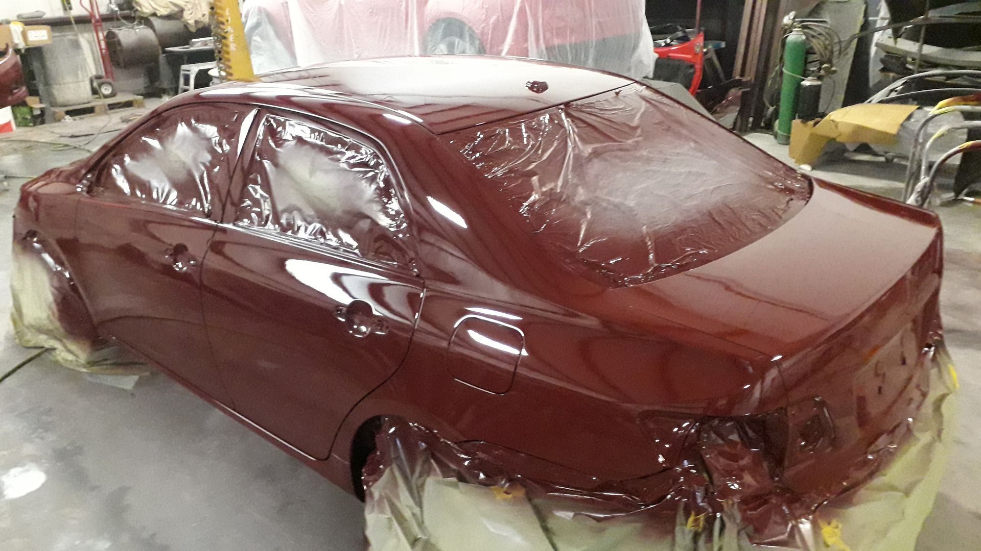 Maroon car body wrapped in plastic, parked in an auto workshop for painting or repair