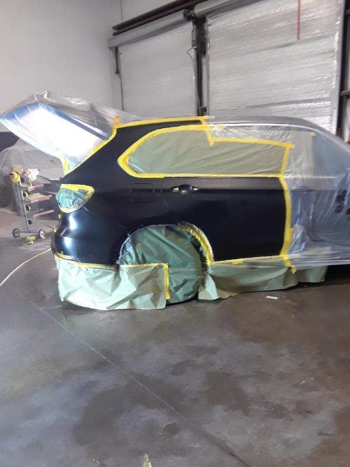 Black SUV in a garage with hood open and windows masked off for painting