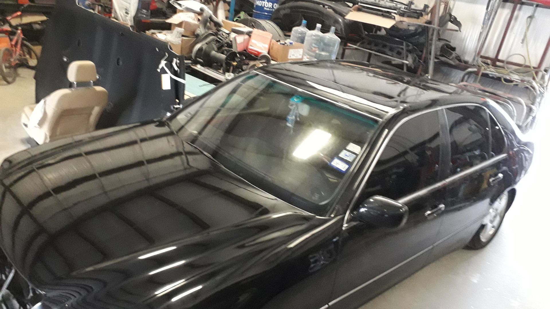 Black sedan parked in a garage beside covered vehicles and shelves of stored items