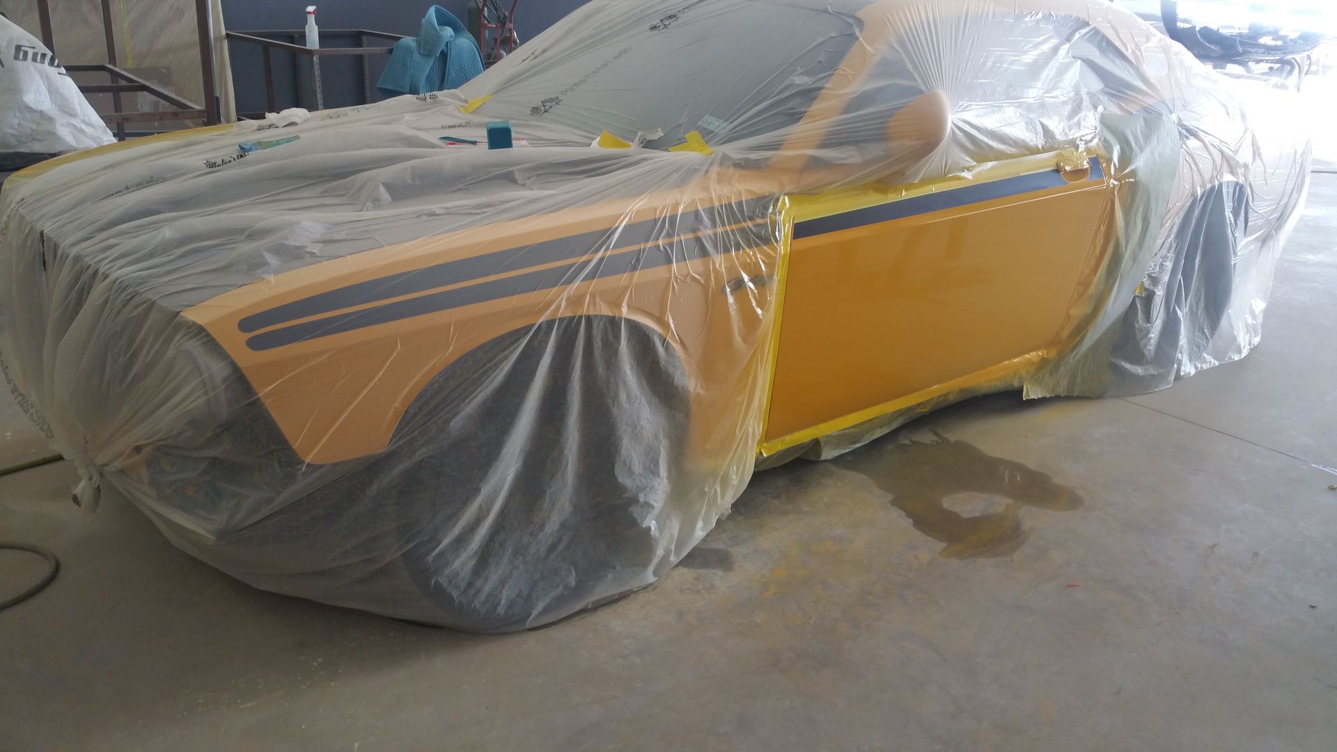 Yellow sports car covered in plastic sheeting in a garage, with gray primer on the front and rear