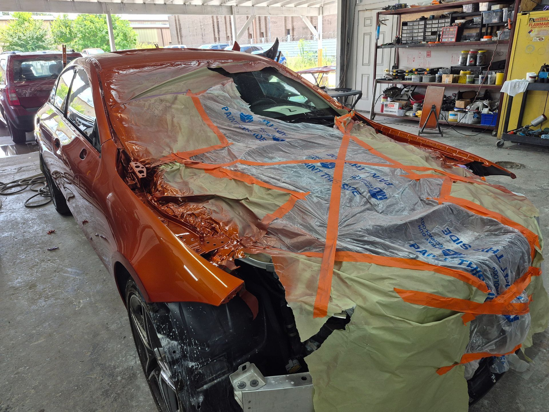 Orange car in a garage, wrapped in plastic and tape for body repair/pain