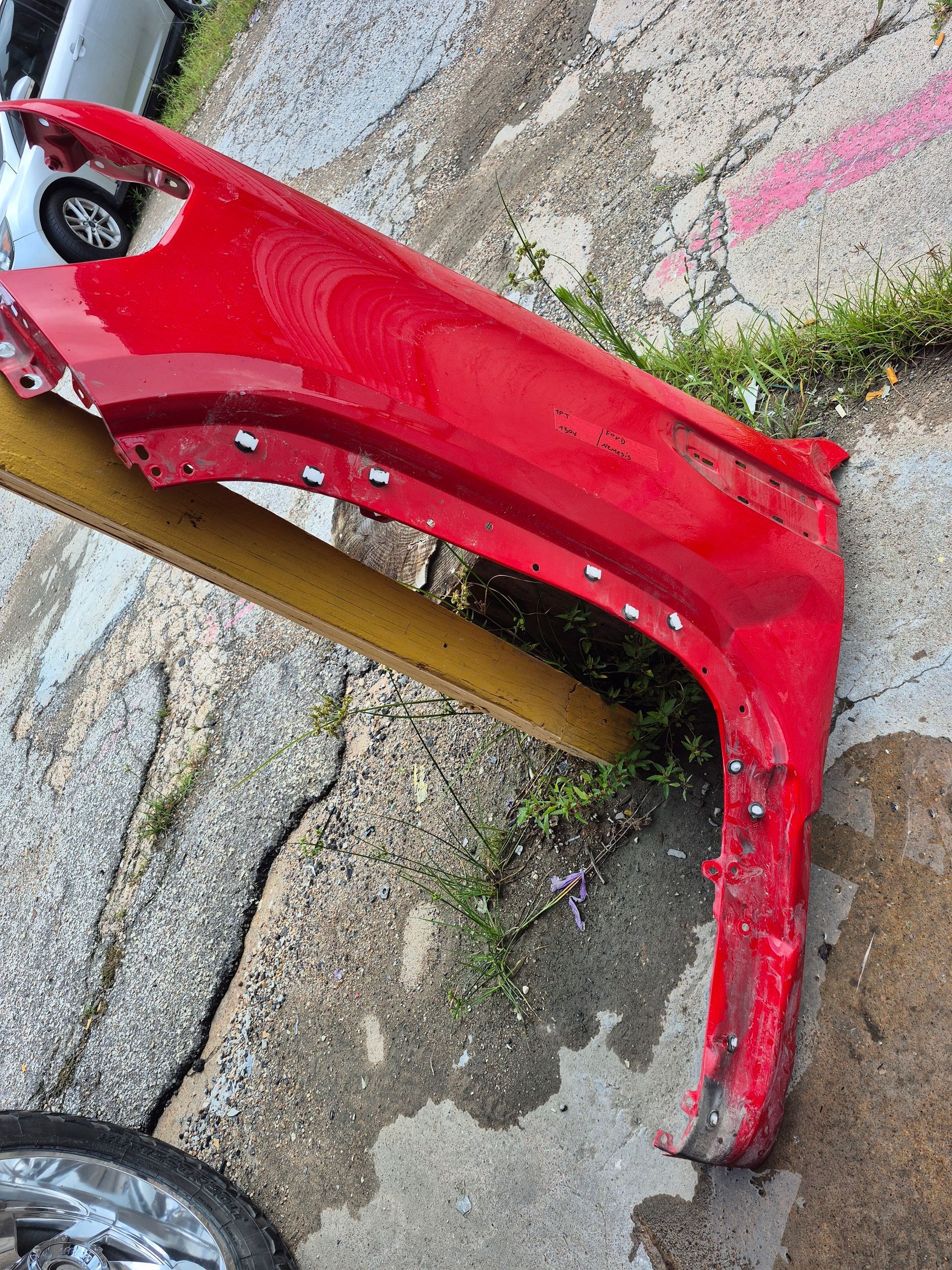 Red car front bumper panel lying on pavement beside a wheel and curb