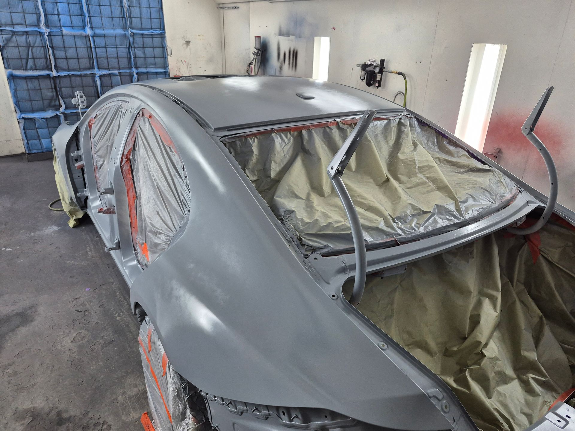Gray car body in a workshop, with windows taped and interior covered in protective plastic.