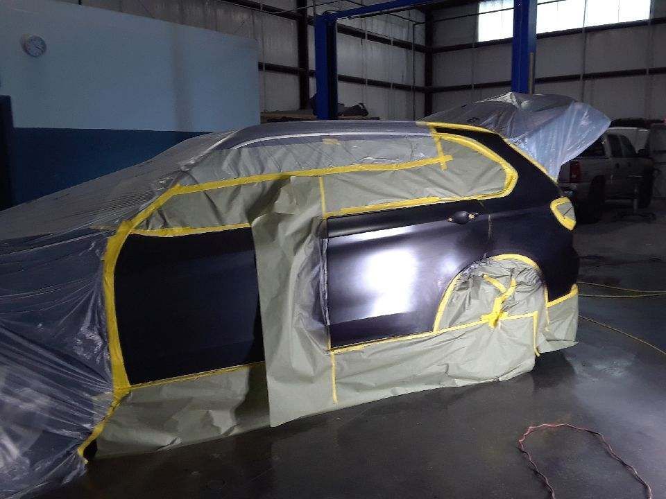 Car masked in plastic and tape inside a workshop, ready for paint refinishing