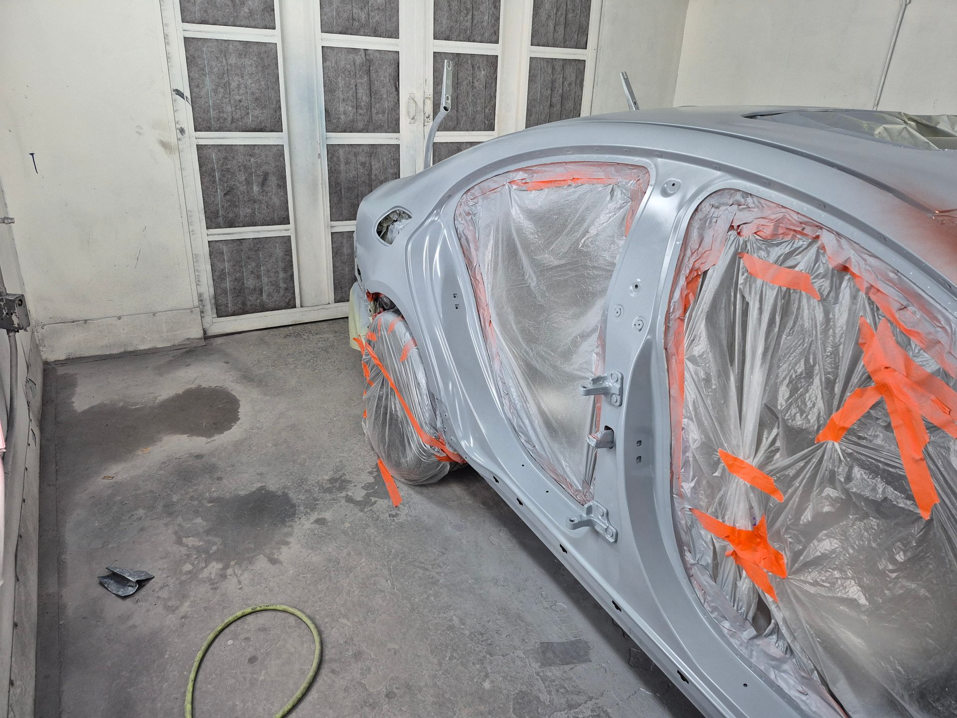 Car with body panels covered in masking tape and plastic in a garage during paint prep