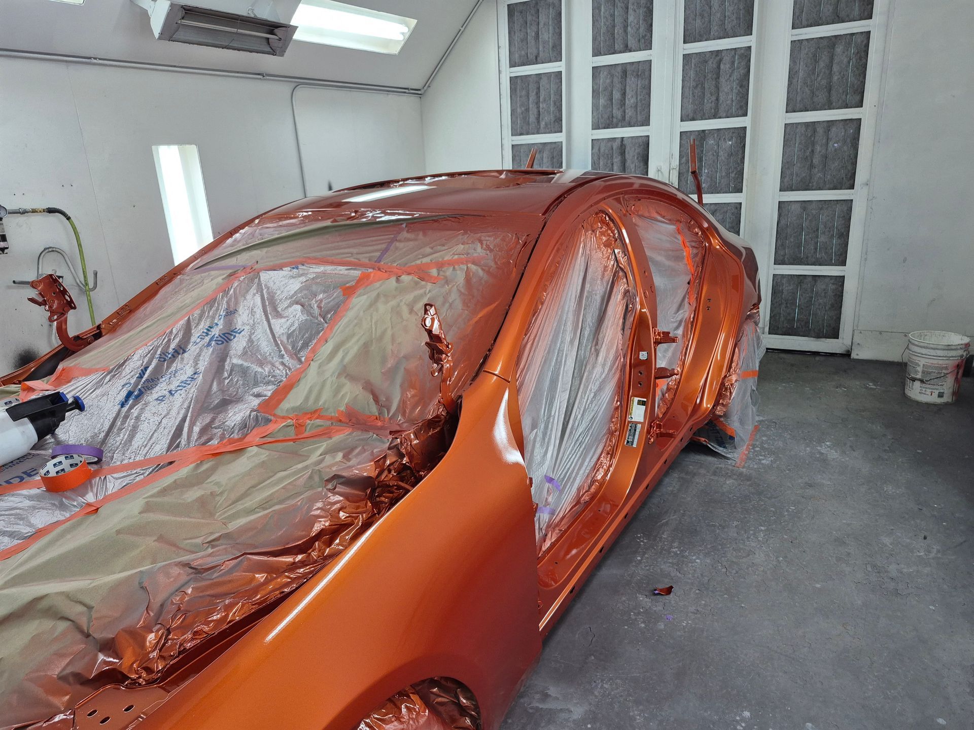 Orange car covered in plastic and masking tape inside a paint booth