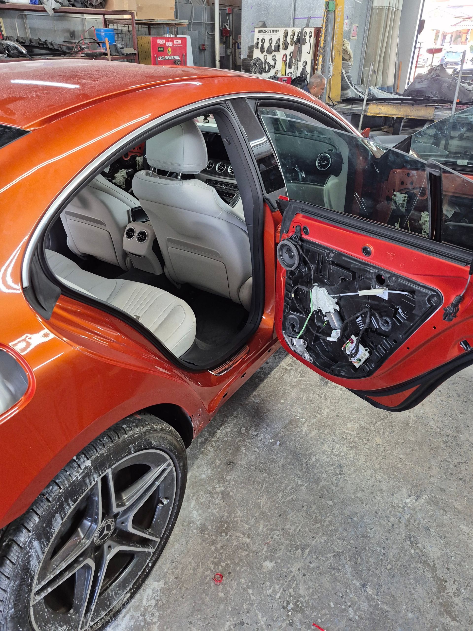 Orange car with open rear door, showing a gray interior and damaged door panel in a garage.