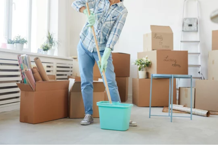 A man is mopping the floor in a living room filled with cardboard boxes.