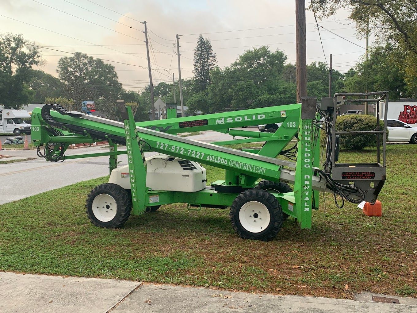 A green and white aerial lift is parked on the side of the road.